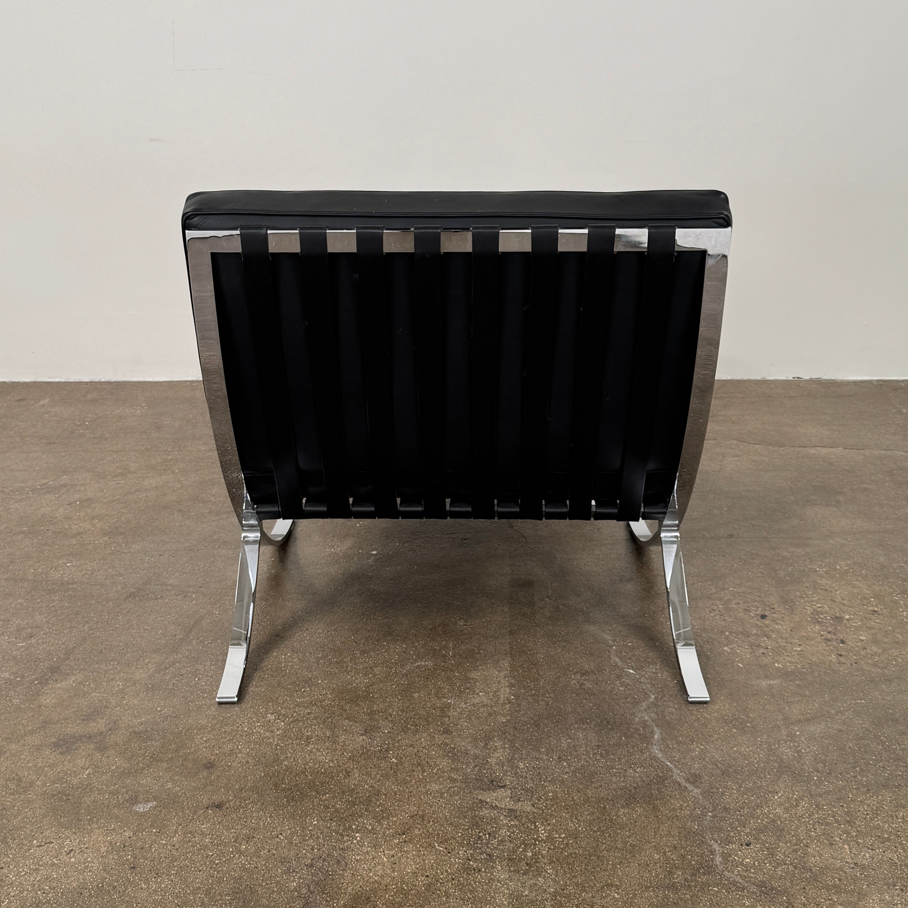 The Vintage DWR Barcelona Black Leather Chair & Ottoman by DWR features button-tufted cushions and chrome X-shaped legs, taking inspiration from the iconic Barcelona Chair, all presented against a plain white background.