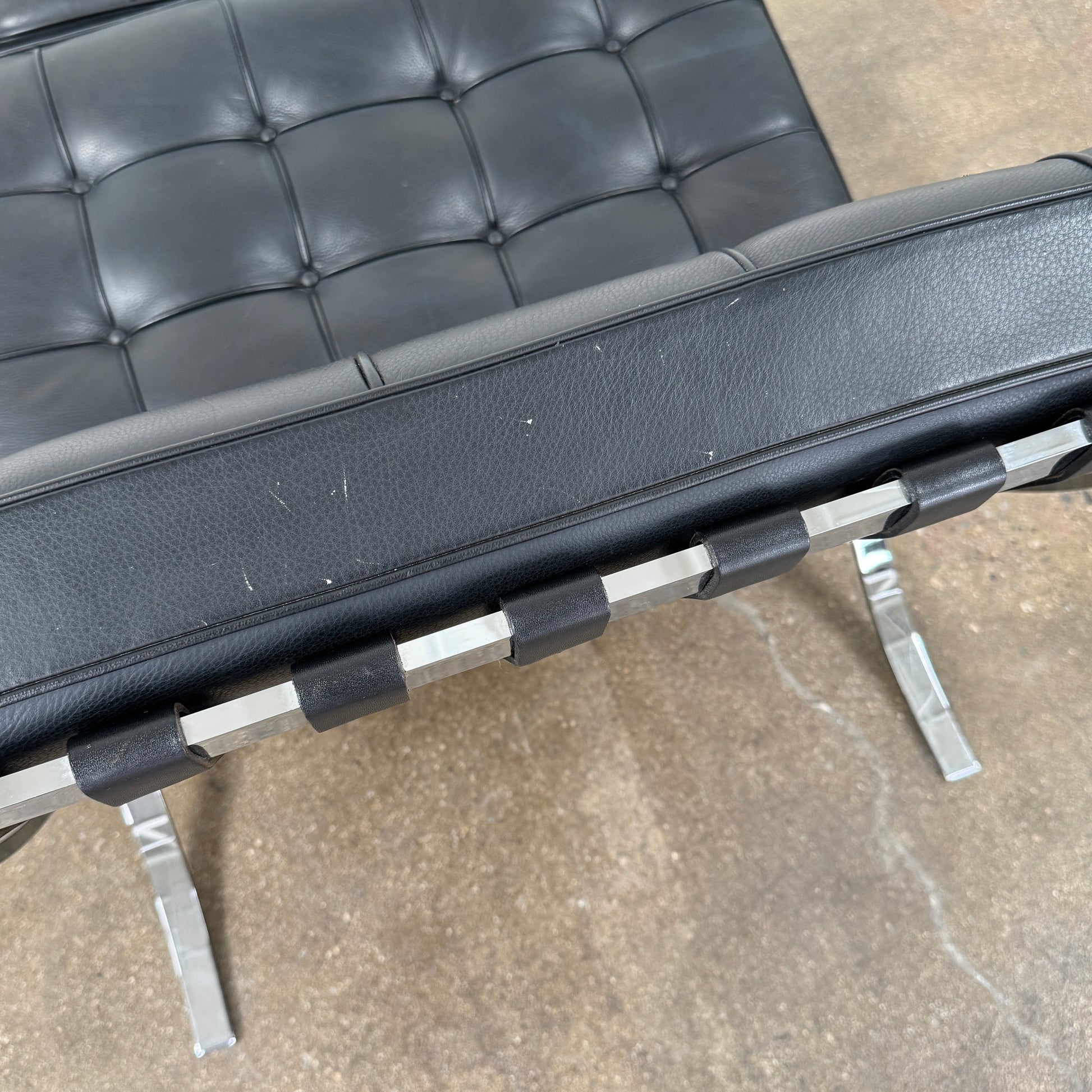 The Vintage DWR Barcelona Black Leather Chair & Ottoman by DWR features button-tufted cushions and chrome X-shaped legs, taking inspiration from the iconic Barcelona Chair, all presented against a plain white background.