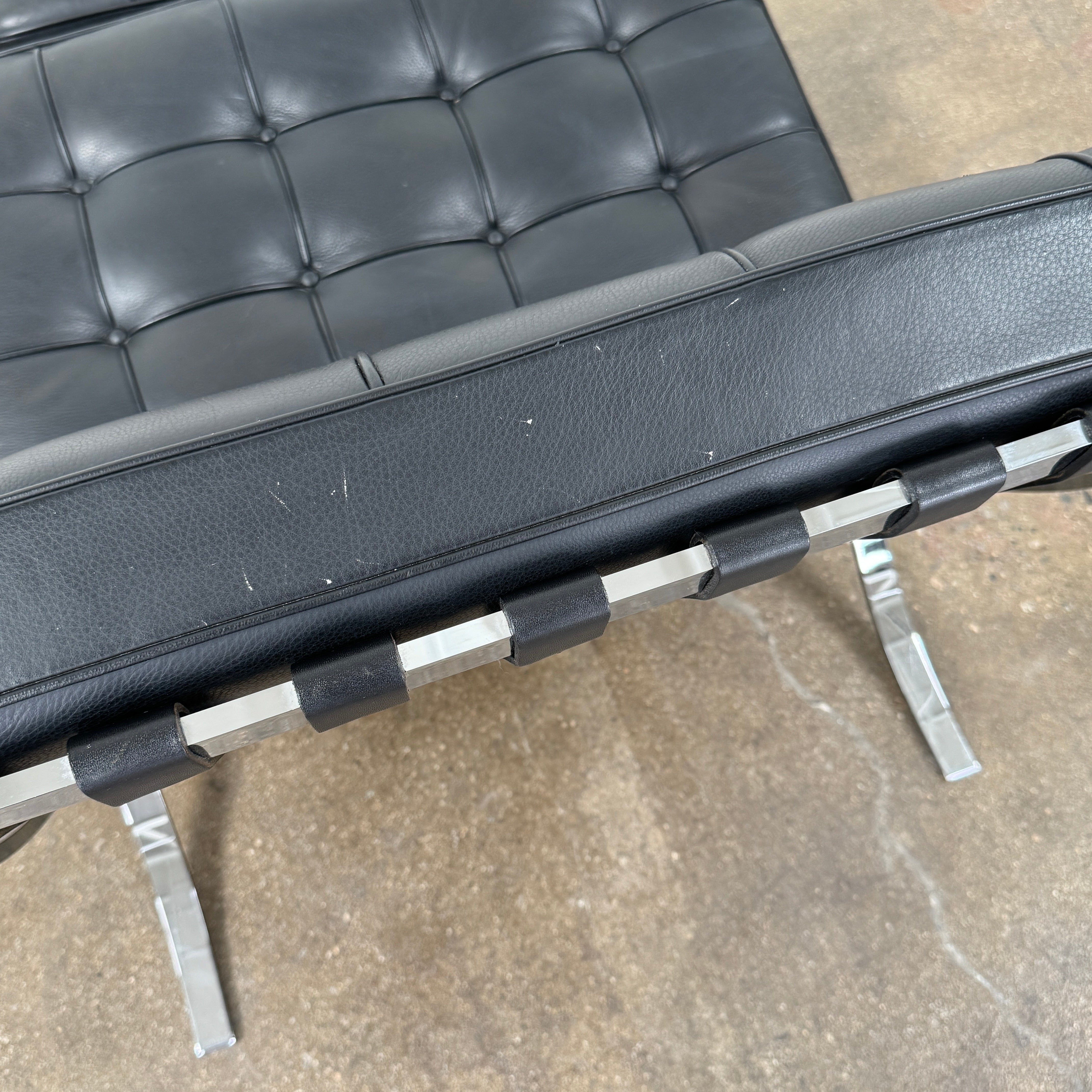 The Vintage DWR Barcelona Black Leather Chair & Ottoman by DWR features button-tufted cushions and chrome X-shaped legs, taking inspiration from the iconic Barcelona Chair, all presented against a plain white background.