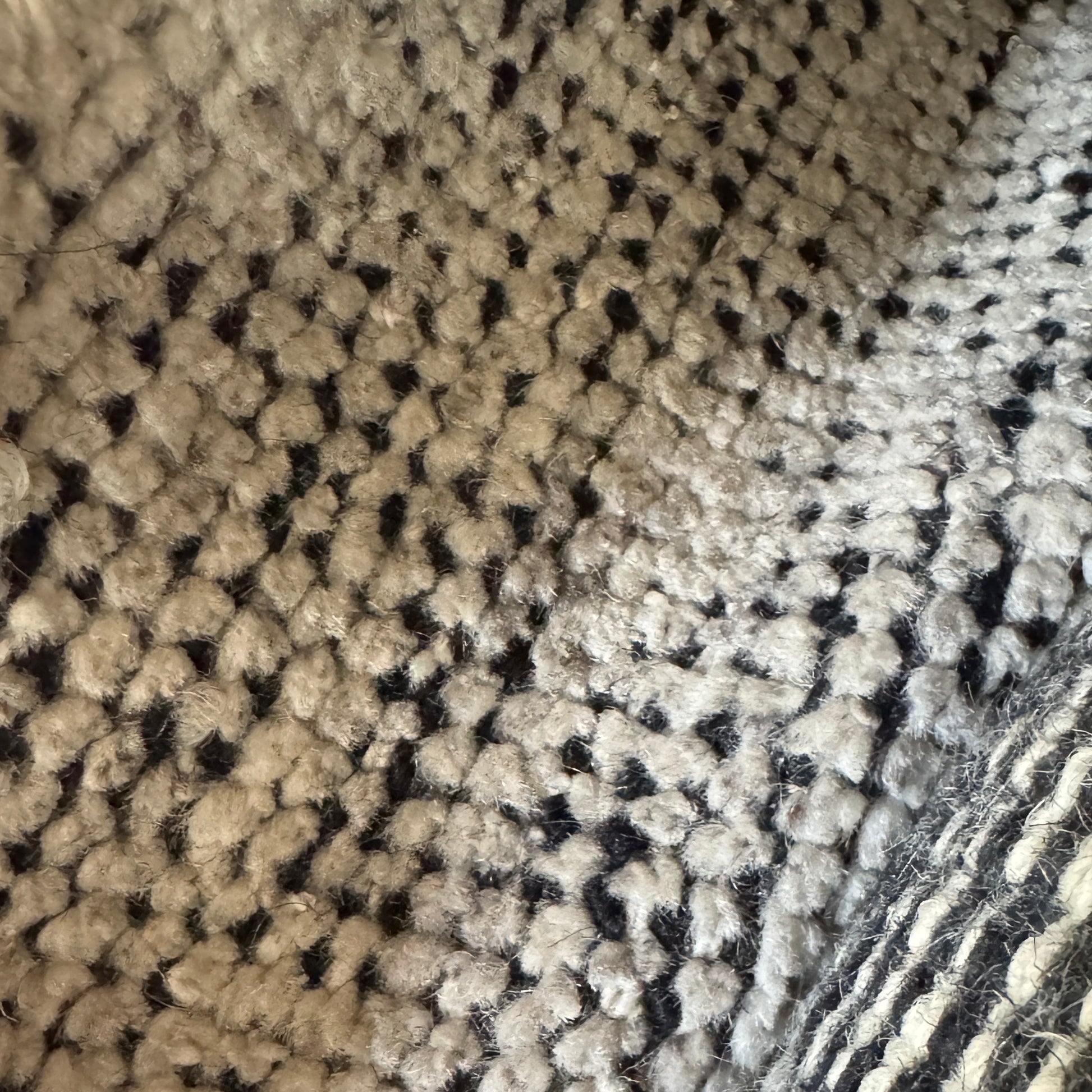 An 8'x10' rectangular DWR Luna Rug in gray with a subtle textured pattern is placed on a concrete floor against a white wall.