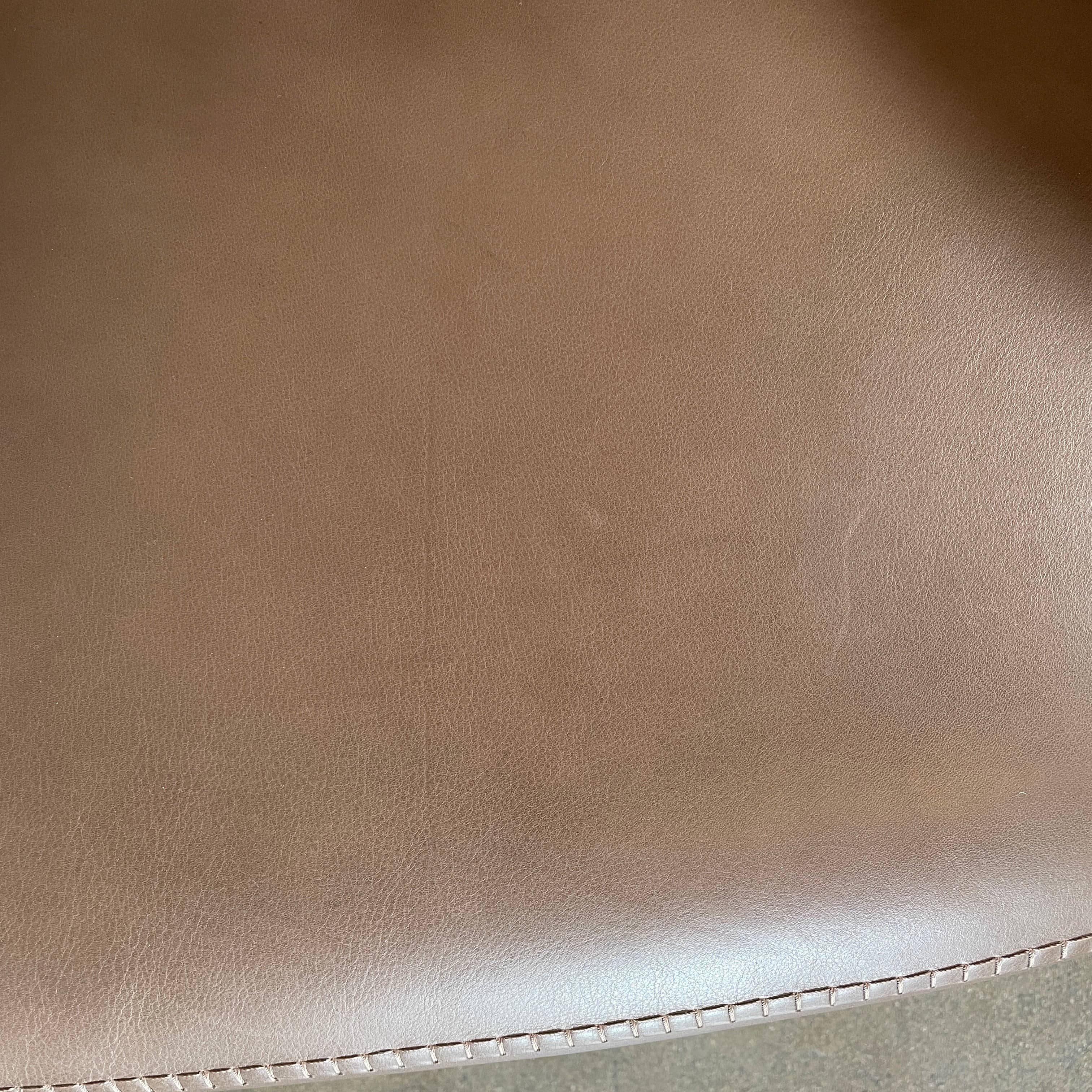 A brown leather armchair with a high backrest and curved arms, showcasing classic leather upholstery, is paired with a matching ottoman, both resting on thin legs. This sophisticated set embodies the elegant style of Maxalto's Maxalto Febo High Back Lounge Chair and Ottoman collection.