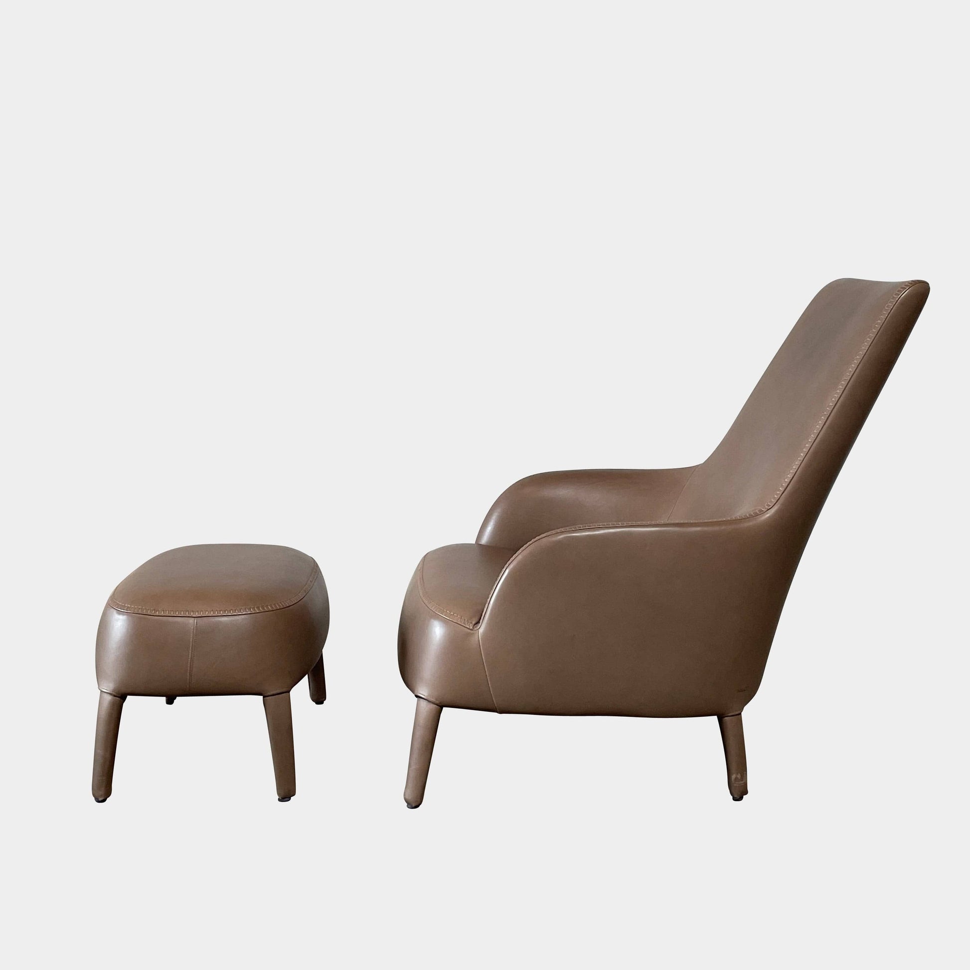 A brown leather armchair with a high backrest and curved arms, showcasing classic leather upholstery, is paired with a matching ottoman, both resting on thin legs. This sophisticated set embodies the elegant style of Maxalto's Maxalto Febo High Back Lounge Chair and Ottoman collection.