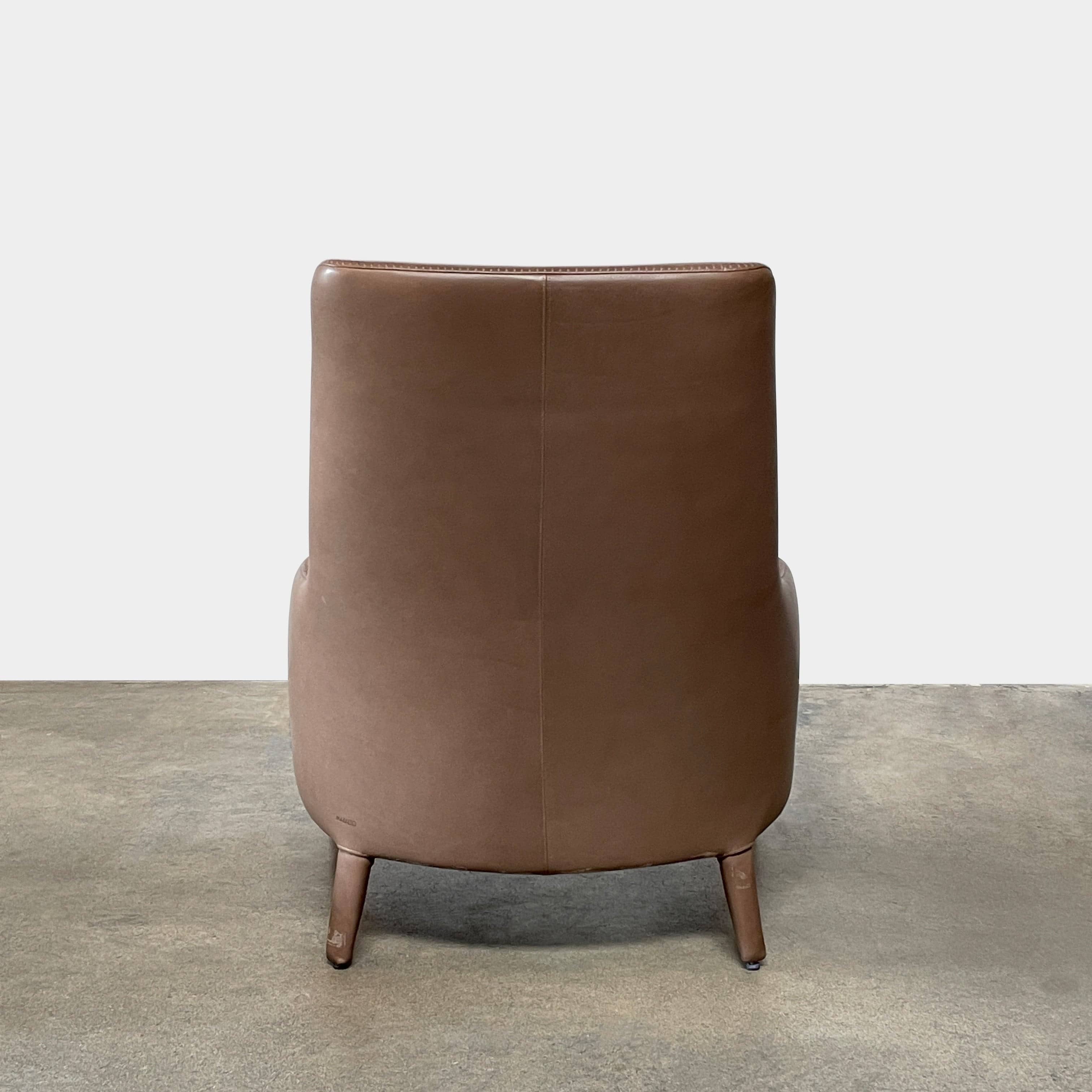 A brown leather armchair with a high backrest and curved arms, showcasing classic leather upholstery, is paired with a matching ottoman, both resting on thin legs. This sophisticated set embodies the elegant style of Maxalto's Maxalto Febo High Back Lounge Chair and Ottoman collection.