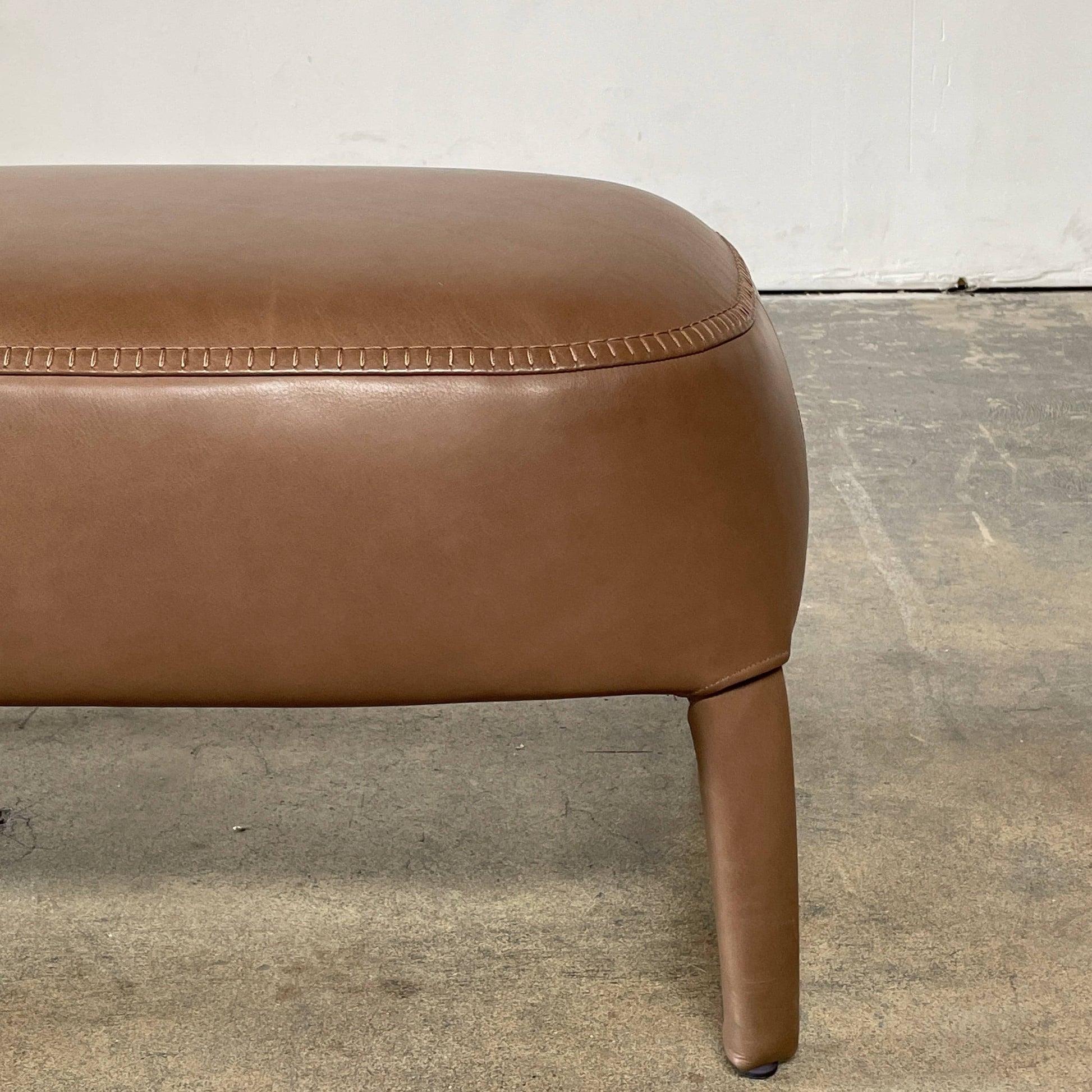 A brown leather armchair with a high backrest and curved arms, showcasing classic leather upholstery, is paired with a matching ottoman, both resting on thin legs. This sophisticated set embodies the elegant style of Maxalto's Maxalto Febo High Back Lounge Chair and Ottoman collection.