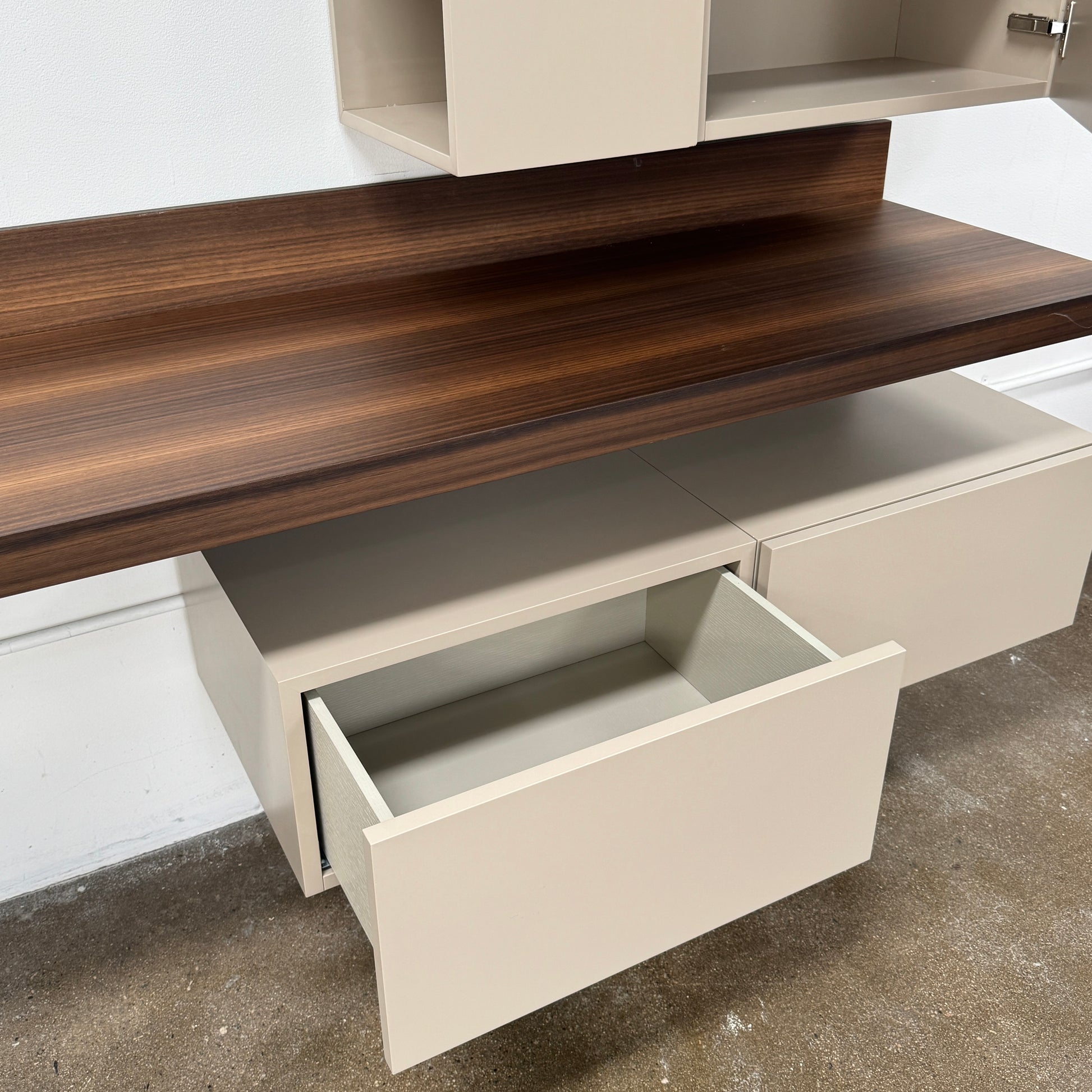 The Molteni & C Fortepiano Wall-mounted Desk System features a long wooden shelf, beige storage cabinets, and drawers for a sleek, modern look against a white wall.
