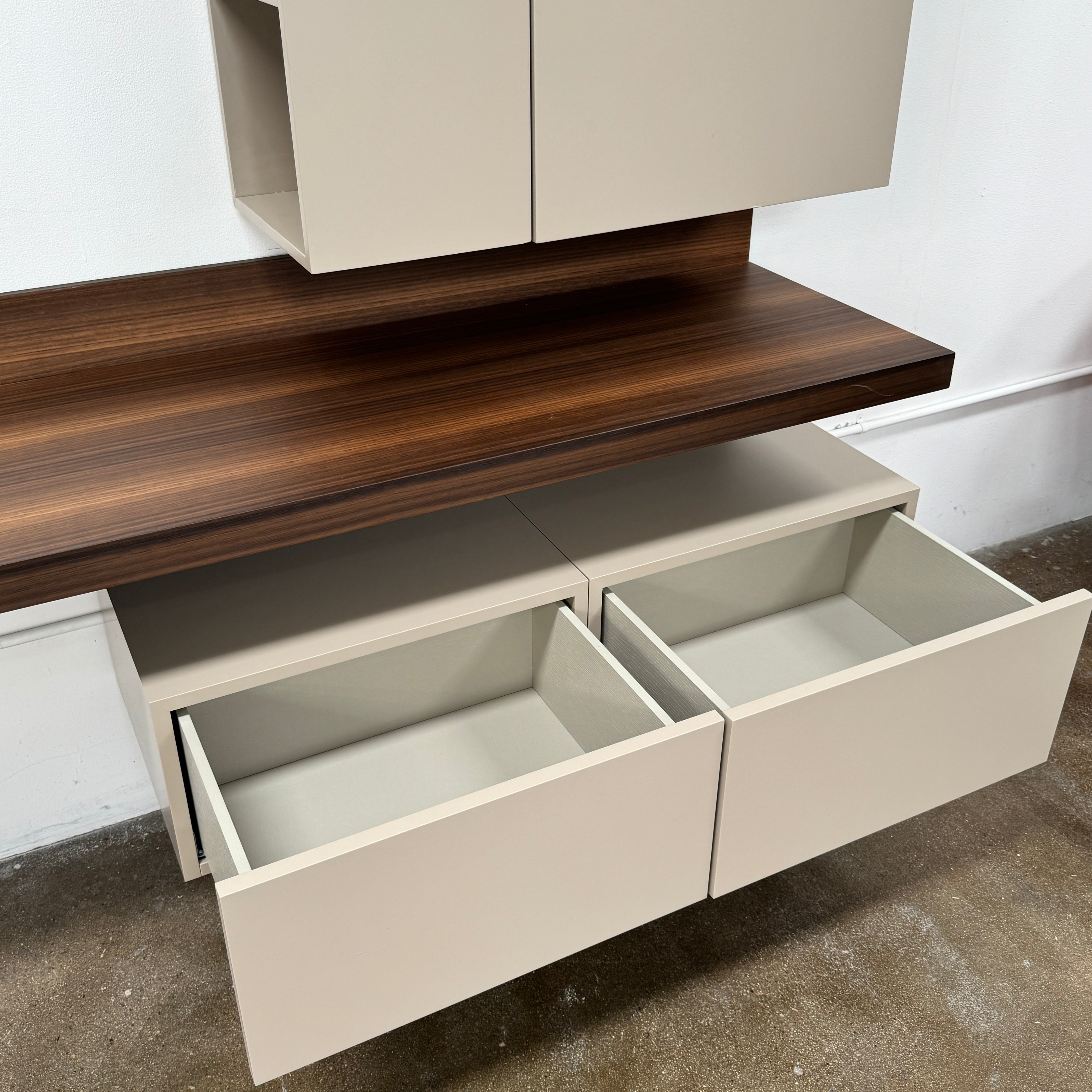 The Molteni & C Fortepiano Wall-mounted Desk System features a long wooden shelf, beige storage cabinets, and drawers for a sleek, modern look against a white wall.