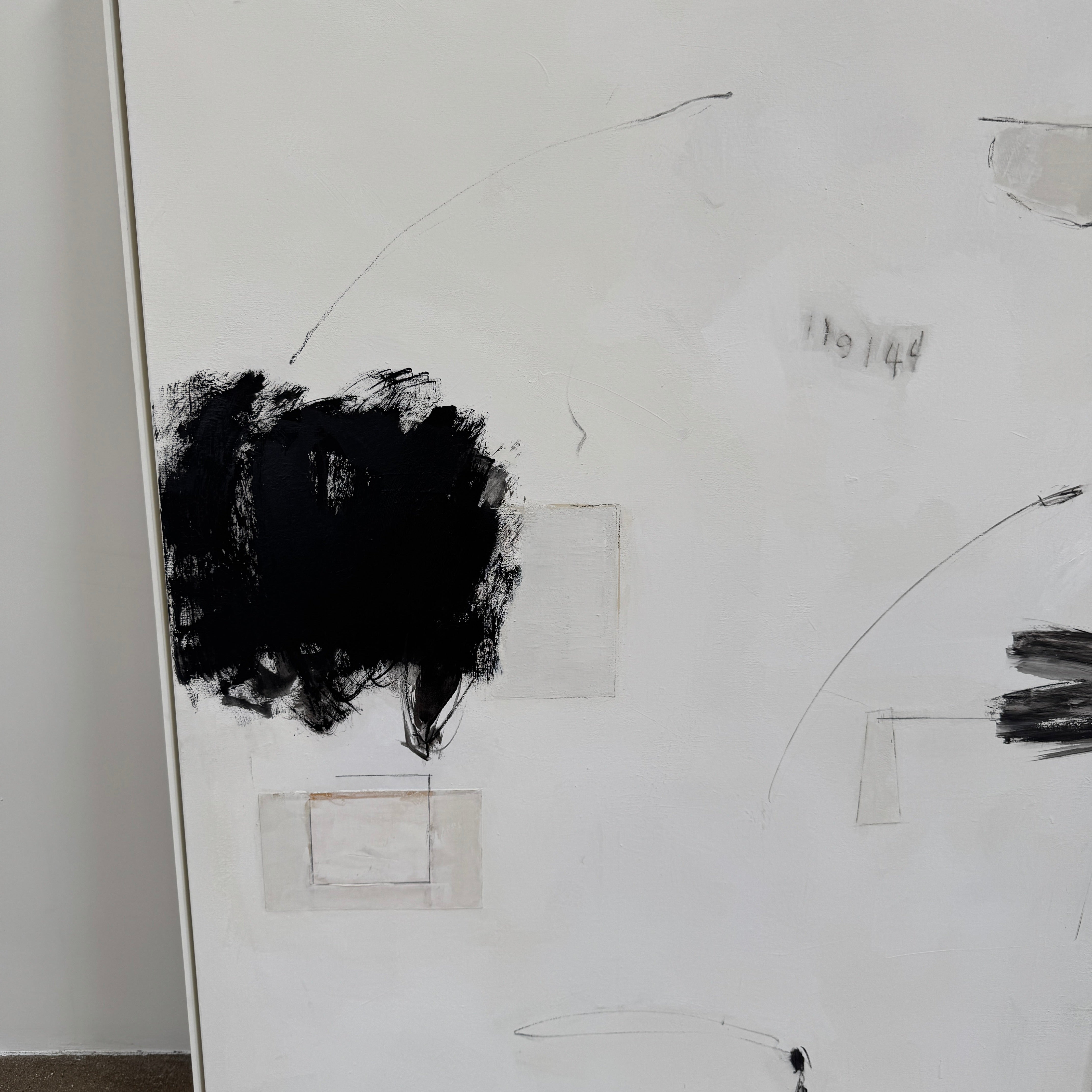 Painting: Abstract by Kimberly Moore from Artist features bold black brush strokes, faint geometric shapes, and subtle lines in black and white, leaning against a white wall on a concrete floor.