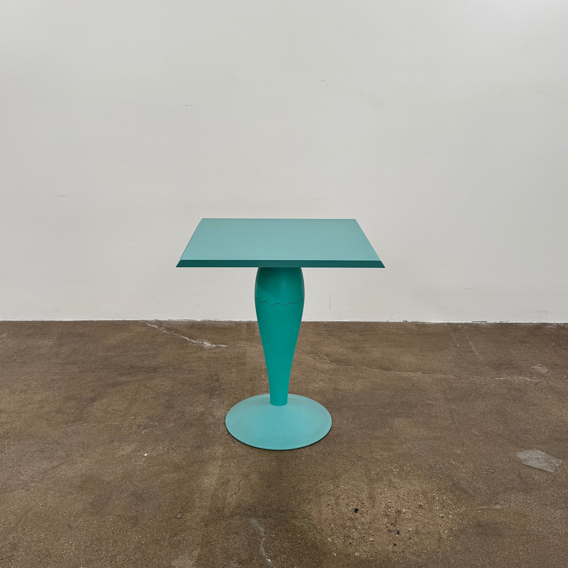 The Vintage Kartell Miss Balu Table by Kartell is a small, square turquoise plastic table with a central pedestal and round base, shown on a plain white background.