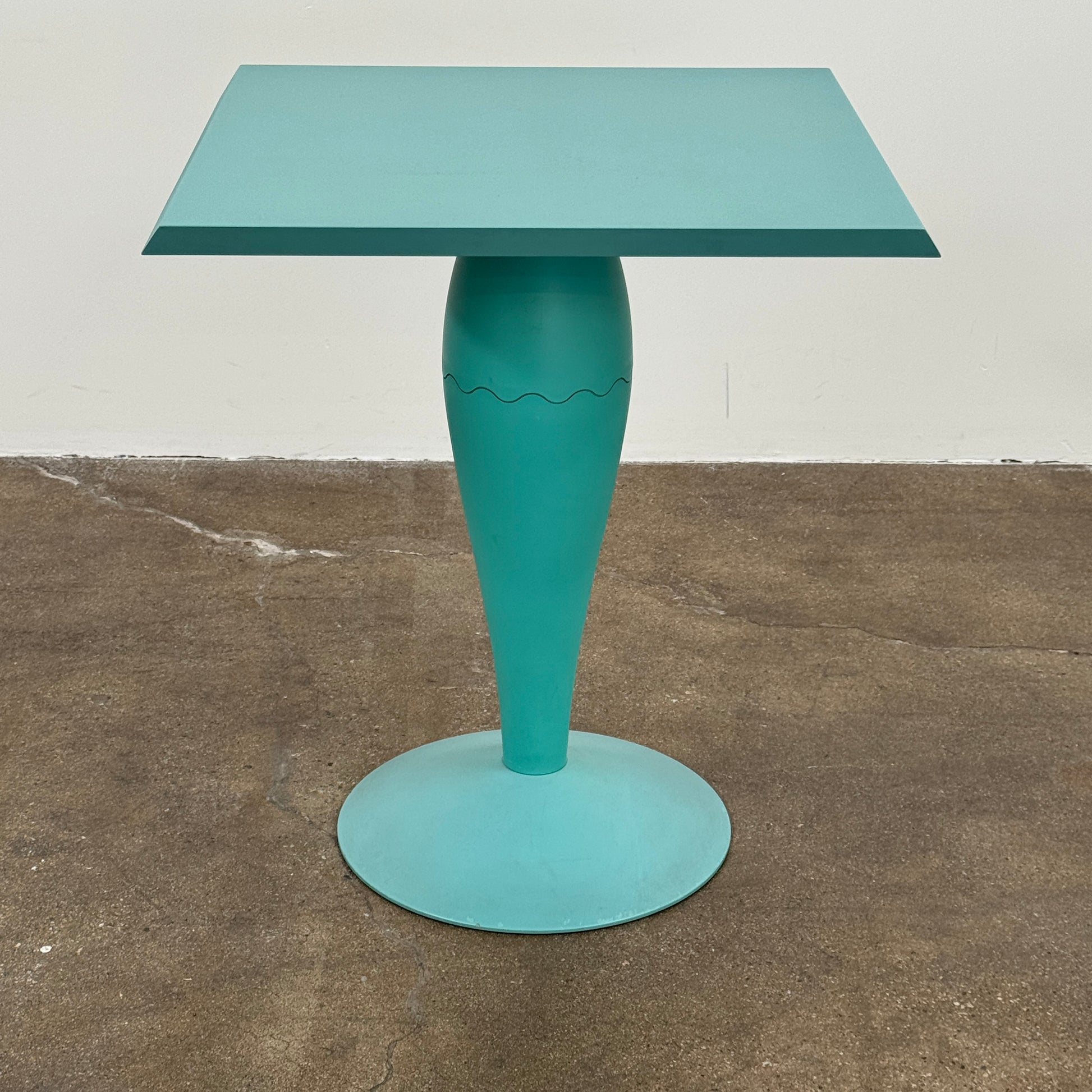 The Vintage Kartell Miss Balu Table by Kartell is a small, square turquoise plastic table with a central pedestal and round base, shown on a plain white background.
