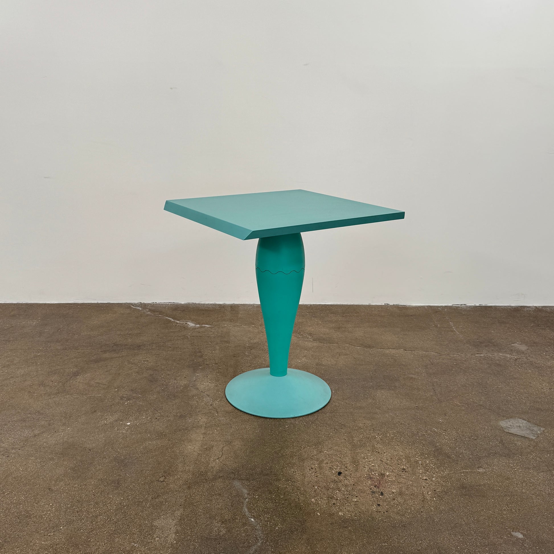 The Vintage Kartell Miss Balu Table by Kartell is a small, square turquoise plastic table with a central pedestal and round base, shown on a plain white background.