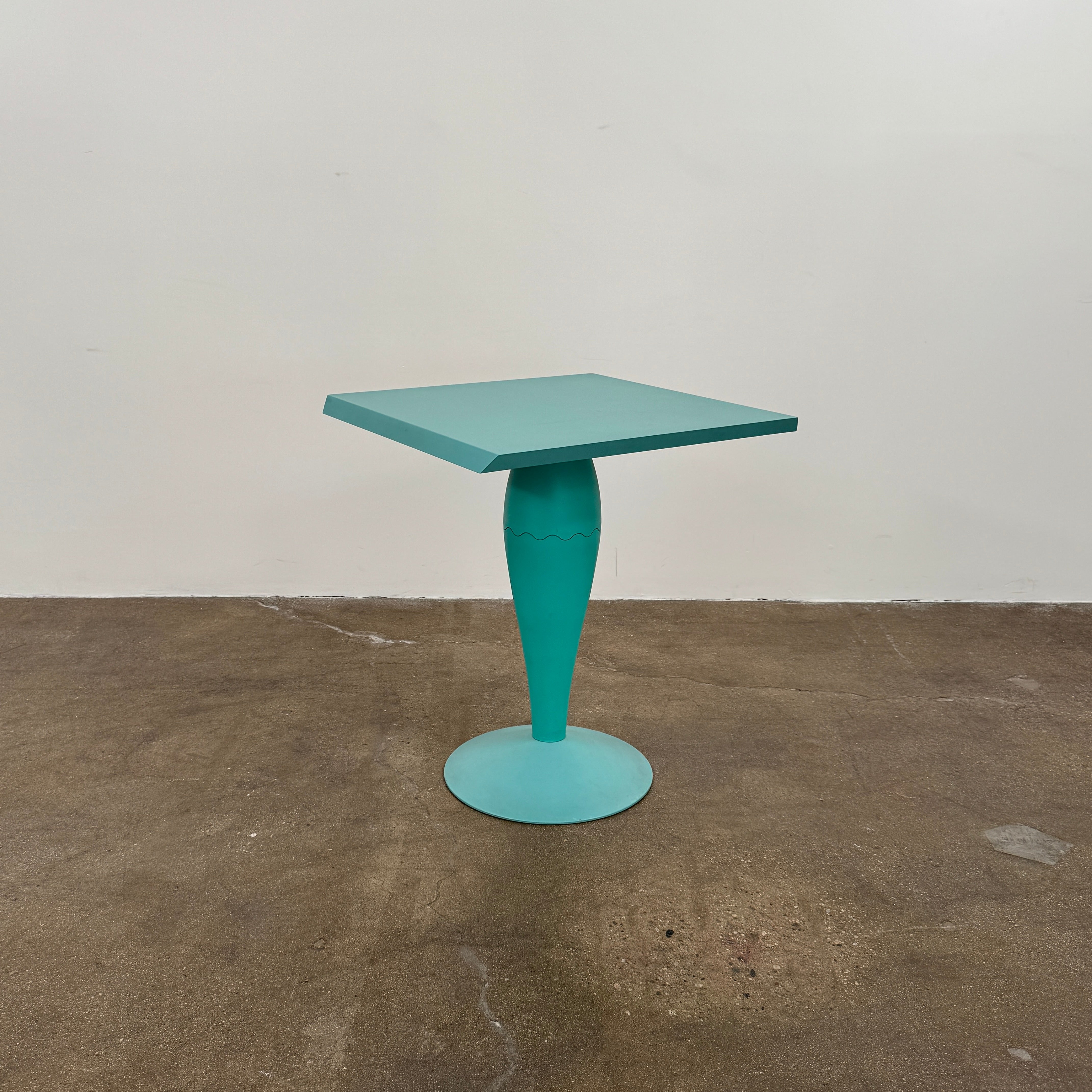 The Vintage Kartell Miss Balu Table by Kartell is a small, square turquoise plastic table with a central pedestal and round base, shown on a plain white background.