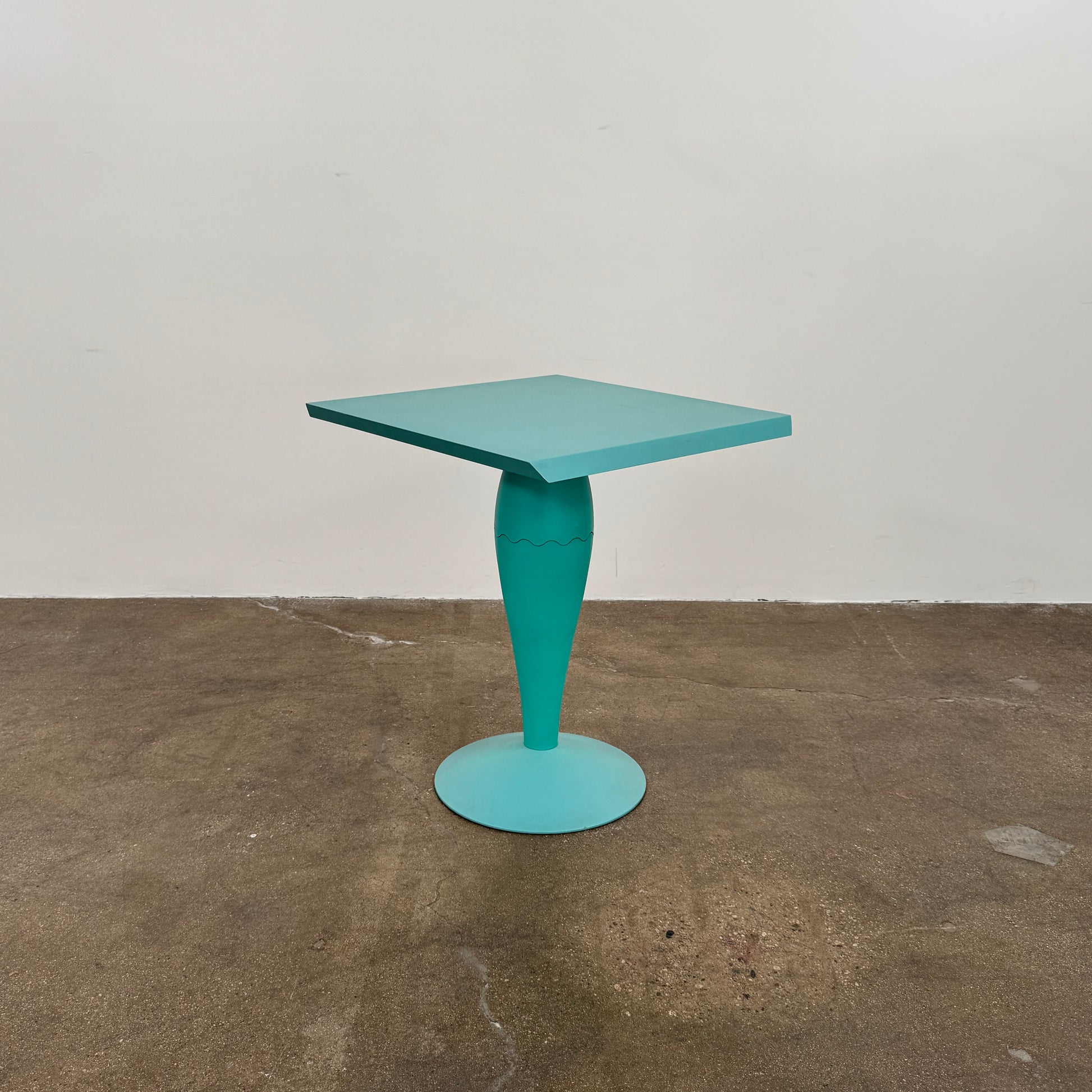 The Vintage Kartell Miss Balu Table by Kartell is a small, square turquoise plastic table with a central pedestal and round base, shown on a plain white background.