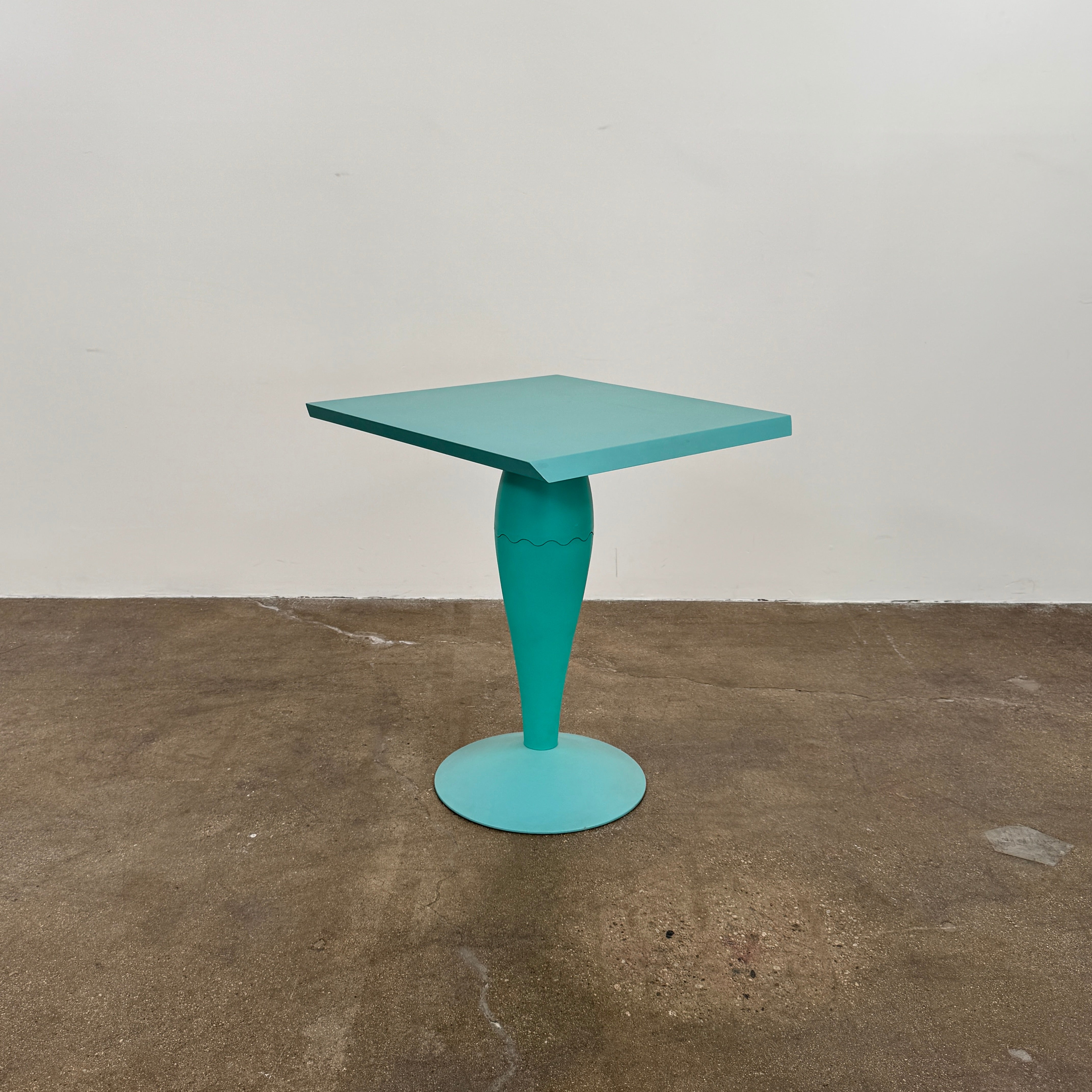 The Vintage Kartell Miss Balu Table by Kartell is a small, square turquoise plastic table with a central pedestal and round base, shown on a plain white background.
