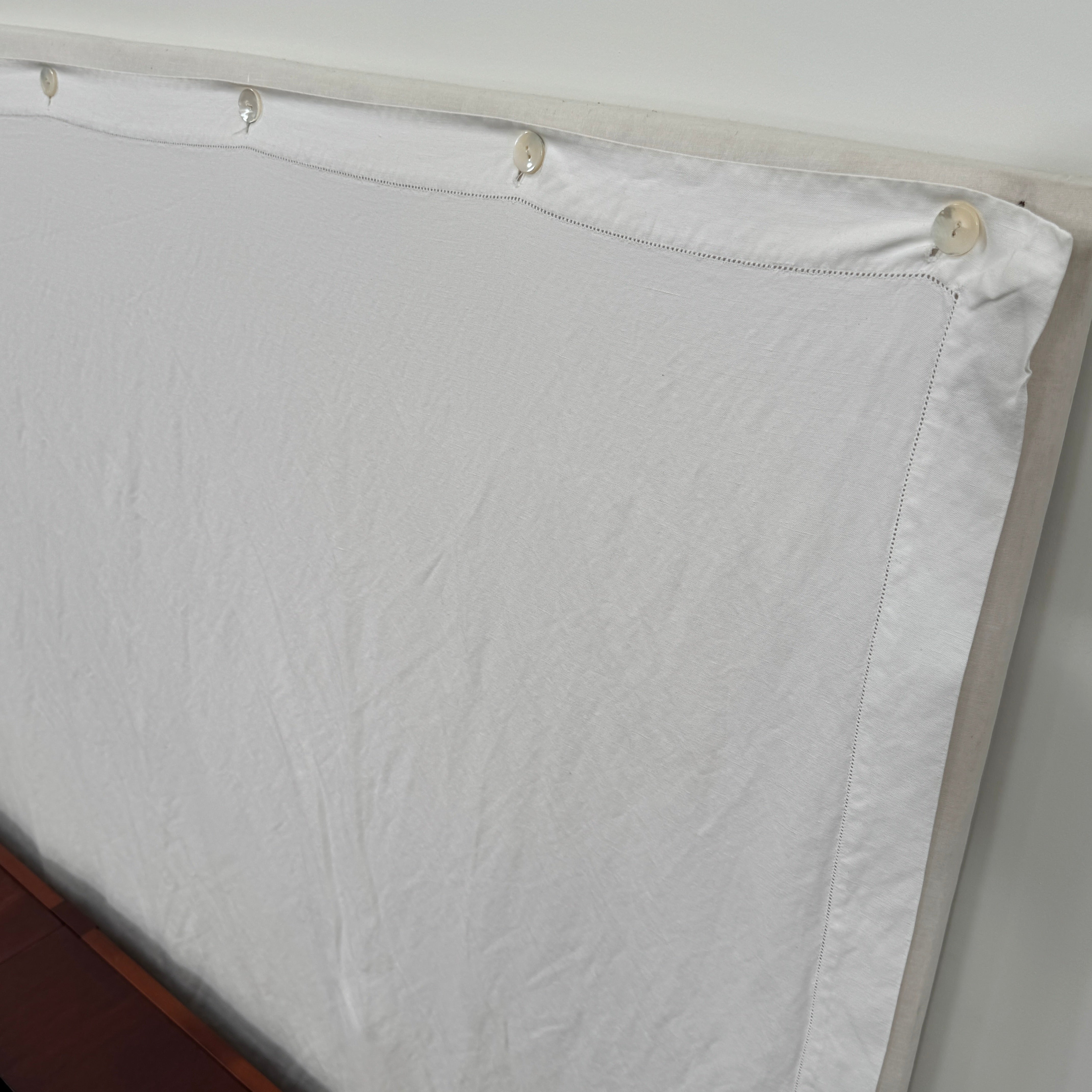 The Driade Neoz European King Size Bed by Driade, featuring wooden slats, wheels, and a white fabric headboard, stands on a concrete floor against a plain white wall.