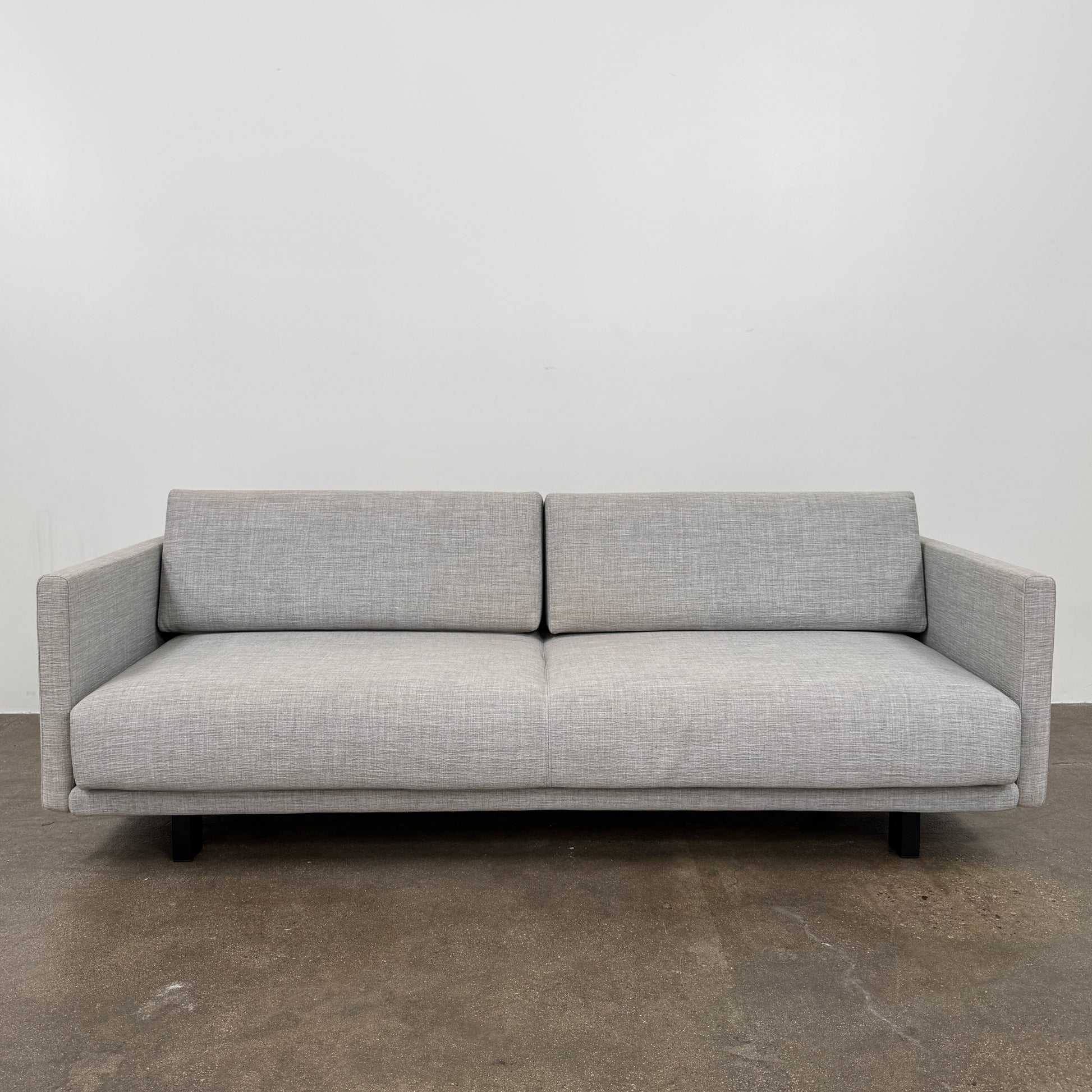 The DWR Tuck Sleeper Sofa by DWR features modern light gray fabric, straight arms, and black legs—ideal for a guest room. Shown against a plain white background.