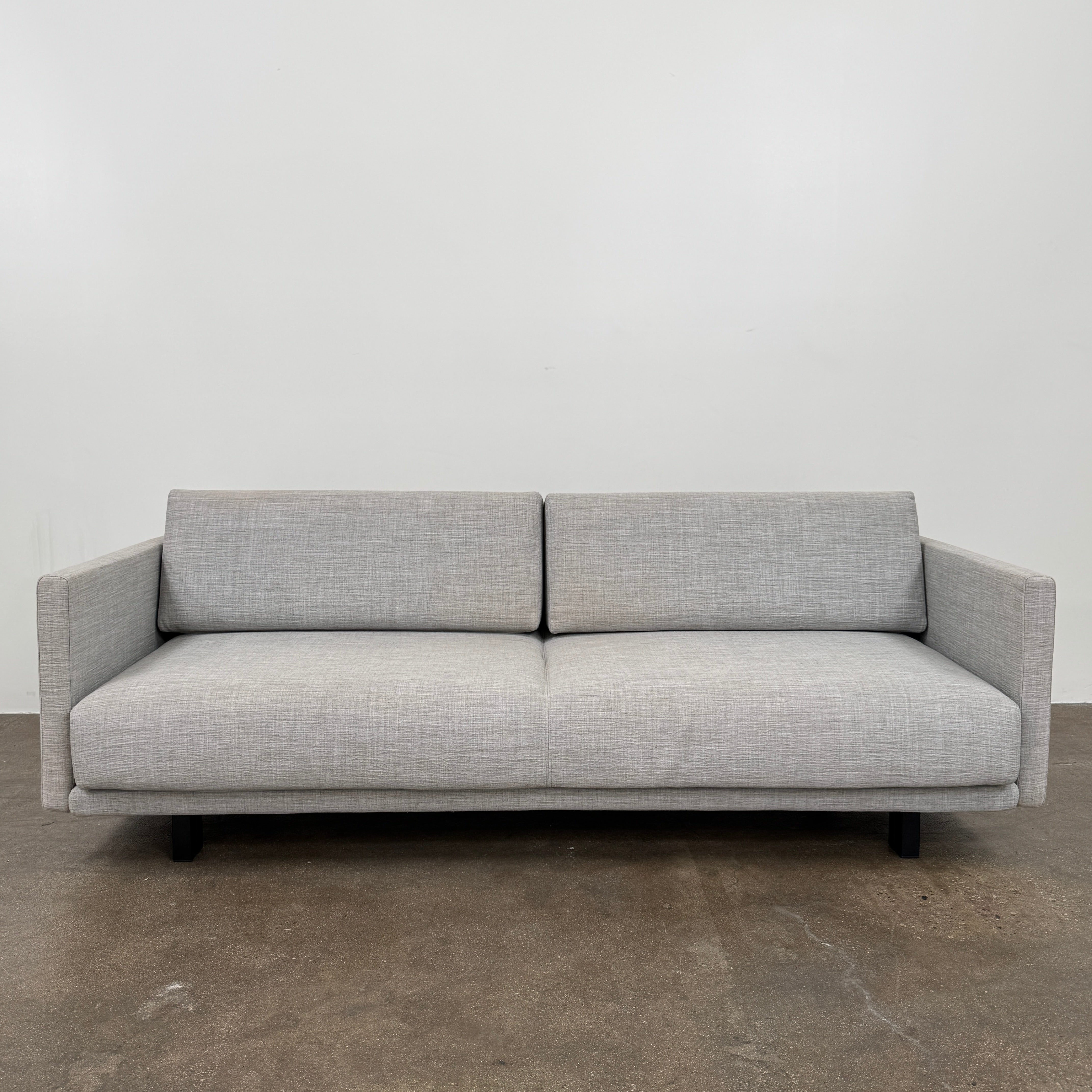 The DWR Tuck Sleeper Sofa by DWR features modern light gray fabric, straight arms, and black legs—ideal for a guest room. Shown against a plain white background.