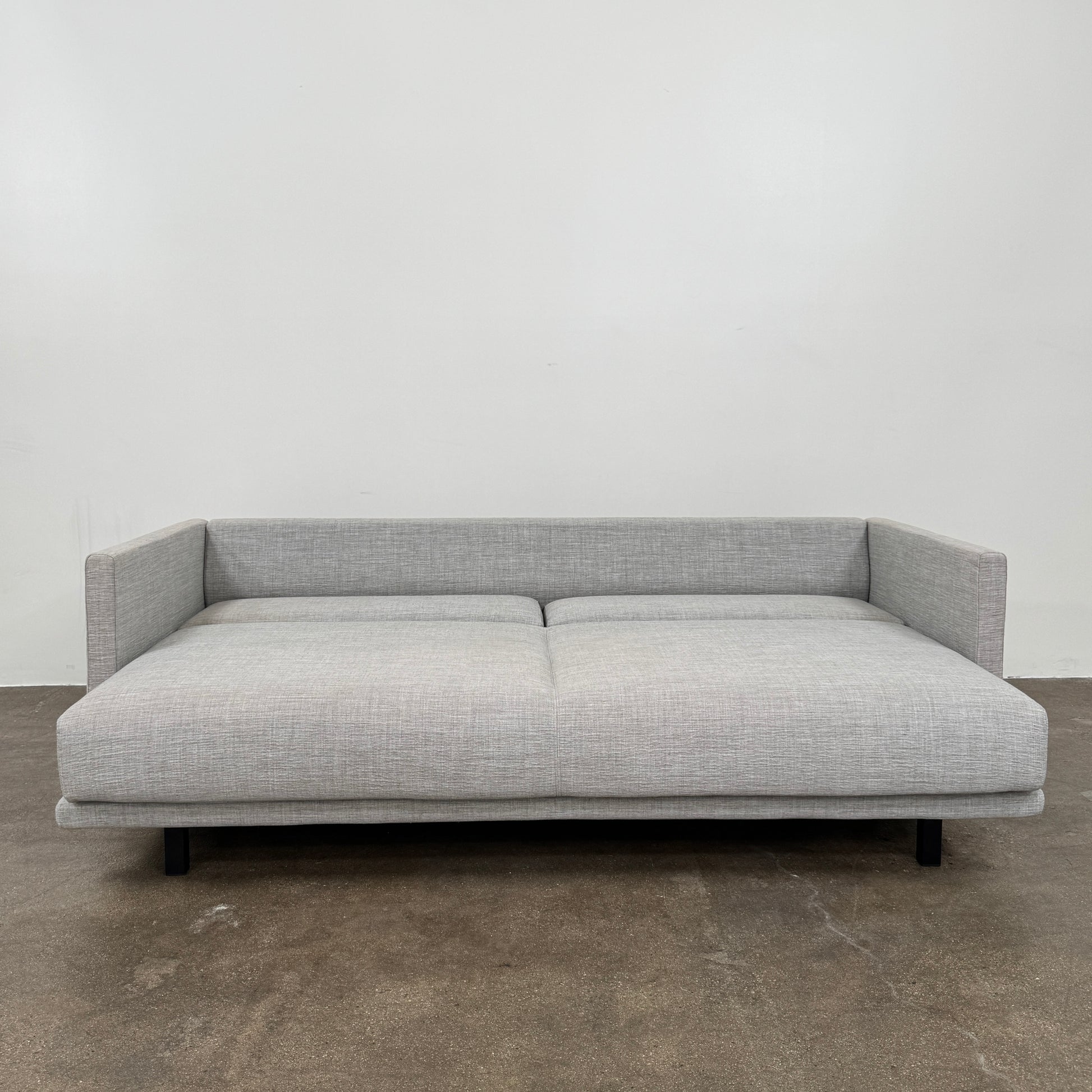 The DWR Tuck Sleeper Sofa by DWR features modern light gray fabric, straight arms, and black legs—ideal for a guest room. Shown against a plain white background.