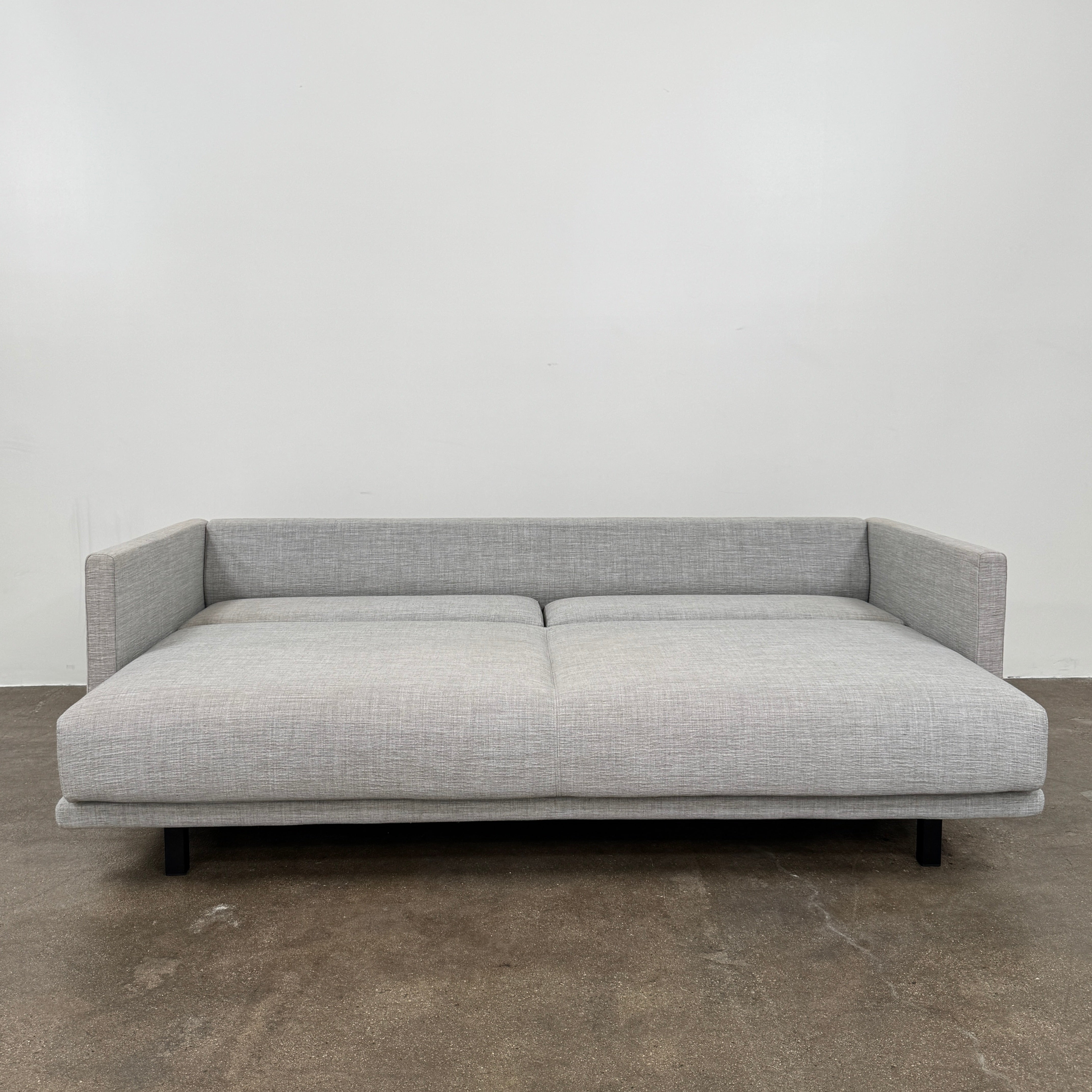 The DWR Tuck Sleeper Sofa by DWR features modern light gray fabric, straight arms, and black legs—ideal for a guest room. Shown against a plain white background.