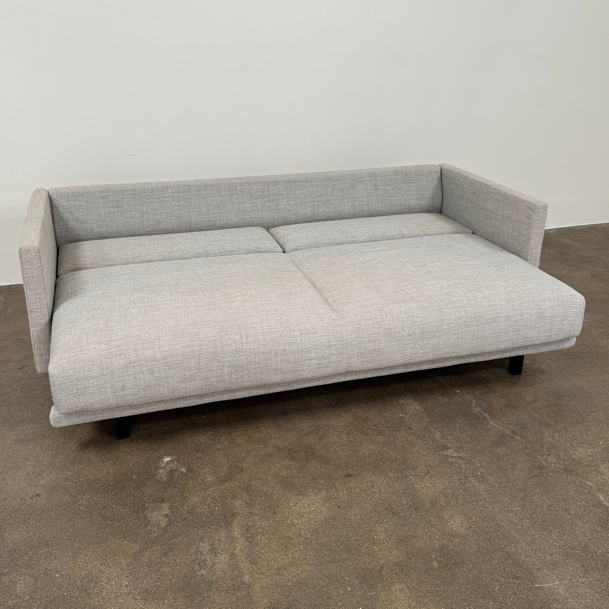 The DWR Tuck Sleeper Sofa by DWR features modern light gray fabric, straight arms, and black legs—ideal for a guest room. Shown against a plain white background.