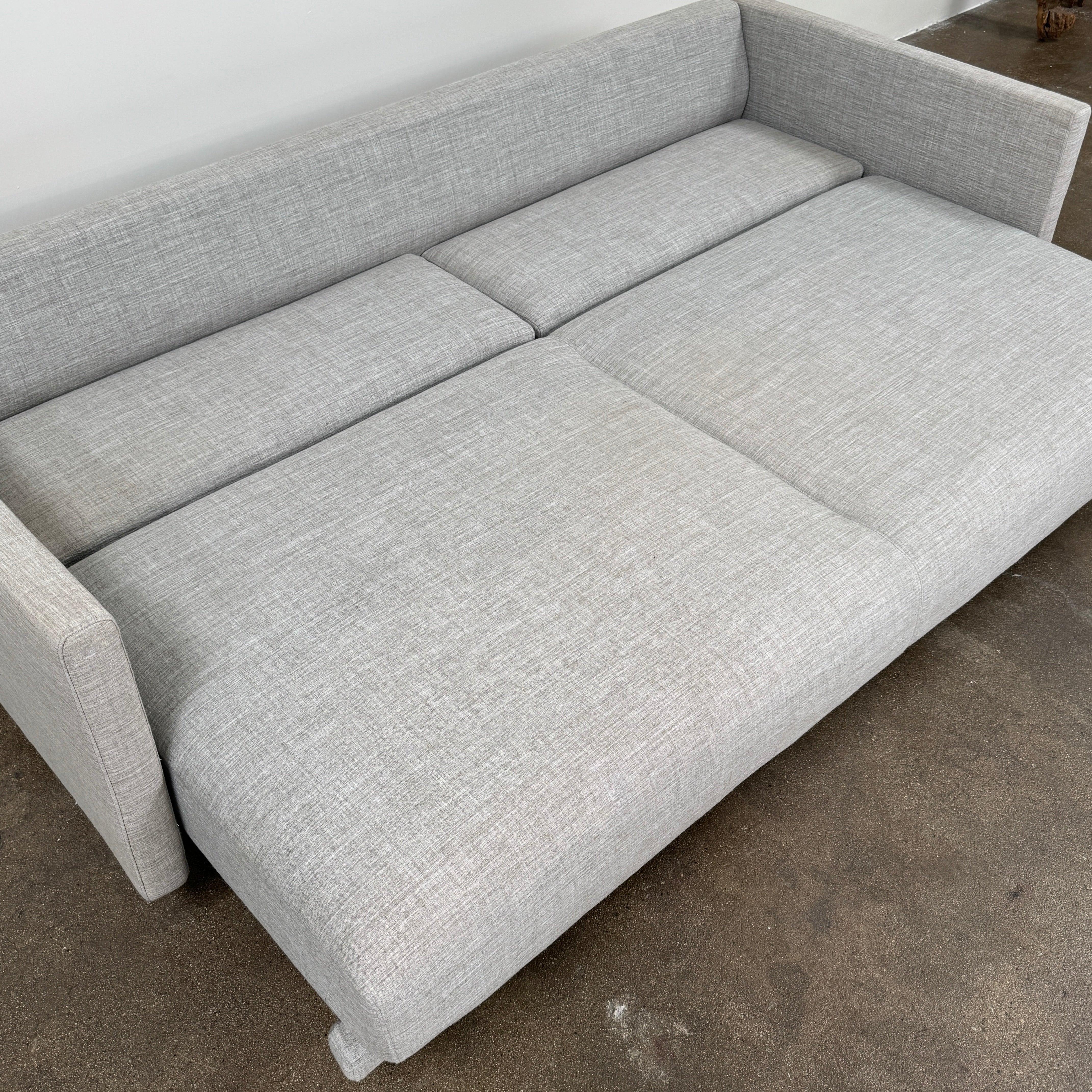 The DWR Tuck Sleeper Sofa by DWR features modern light gray fabric, straight arms, and black legs—ideal for a guest room. Shown against a plain white background.