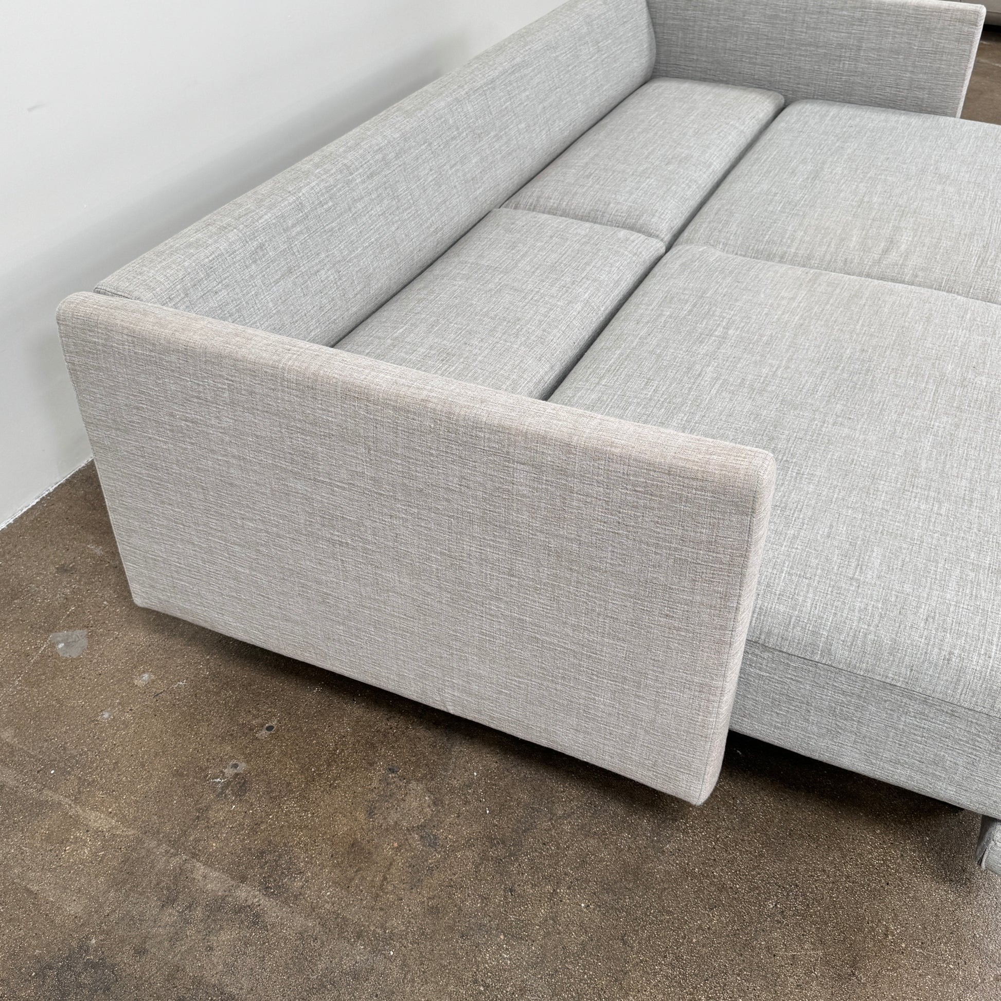 The DWR Tuck Sleeper Sofa by DWR features modern light gray fabric, straight arms, and black legs—ideal for a guest room. Shown against a plain white background.