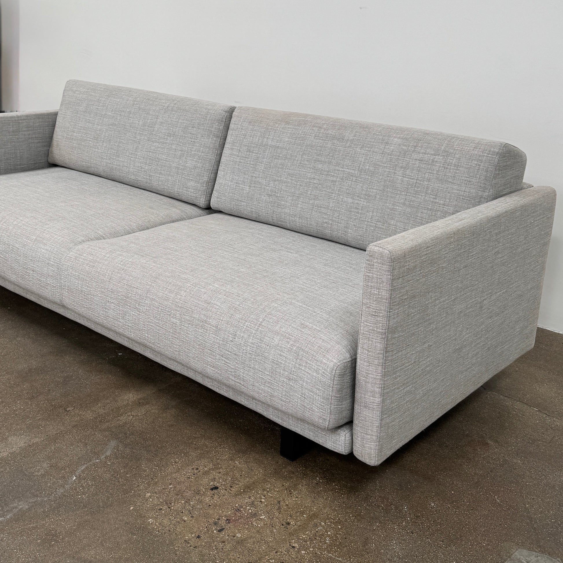 The DWR Tuck Sleeper Sofa by DWR features modern light gray fabric, straight arms, and black legs—ideal for a guest room. Shown against a plain white background.