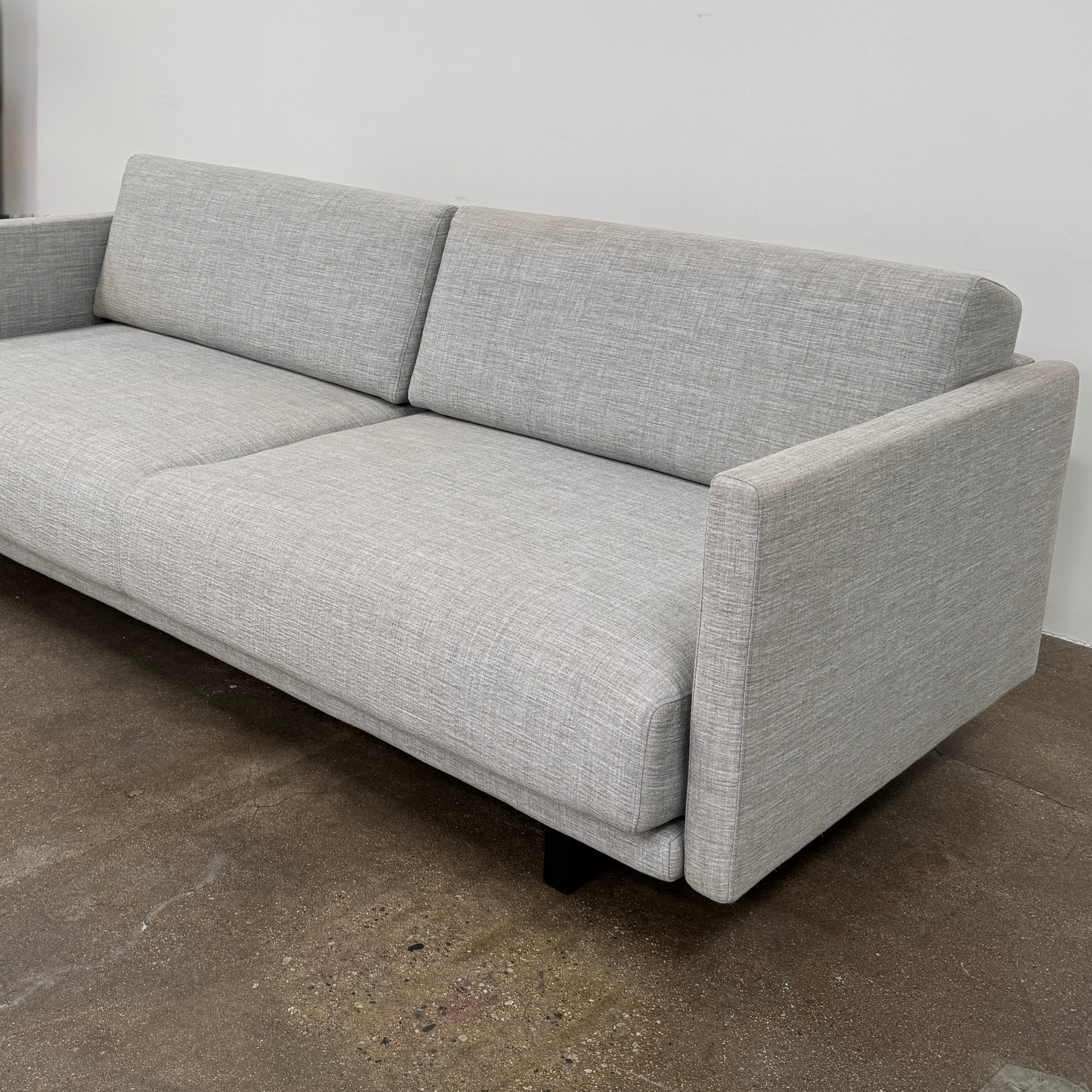 The DWR Tuck Sleeper Sofa by DWR features modern light gray fabric, straight arms, and black legs—ideal for a guest room. Shown against a plain white background.