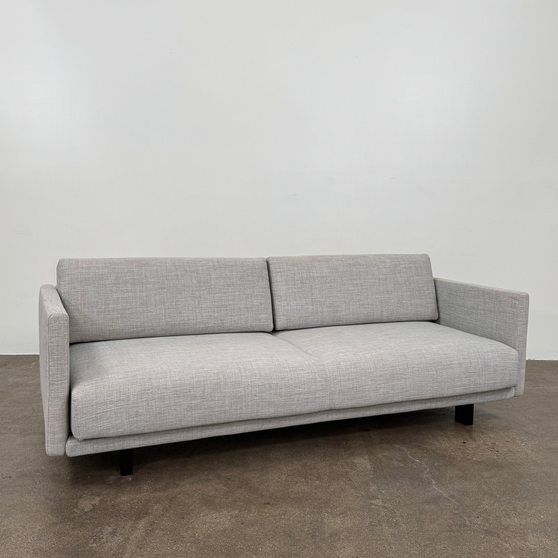 The DWR Tuck Sleeper Sofa by DWR features modern light gray fabric, straight arms, and black legs—ideal for a guest room. Shown against a plain white background.