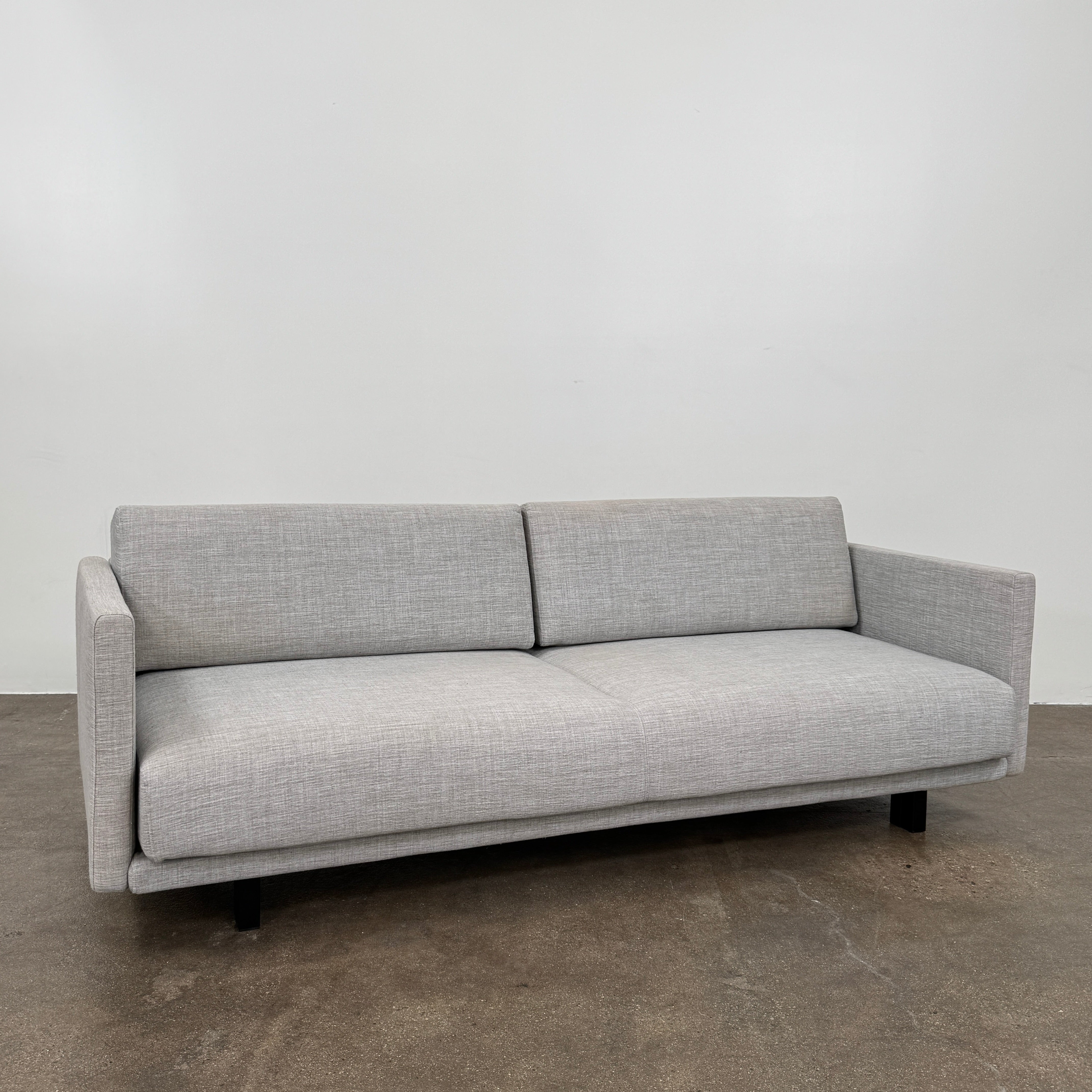 The DWR Tuck Sleeper Sofa by DWR features modern light gray fabric, straight arms, and black legs—ideal for a guest room. Shown against a plain white background.
