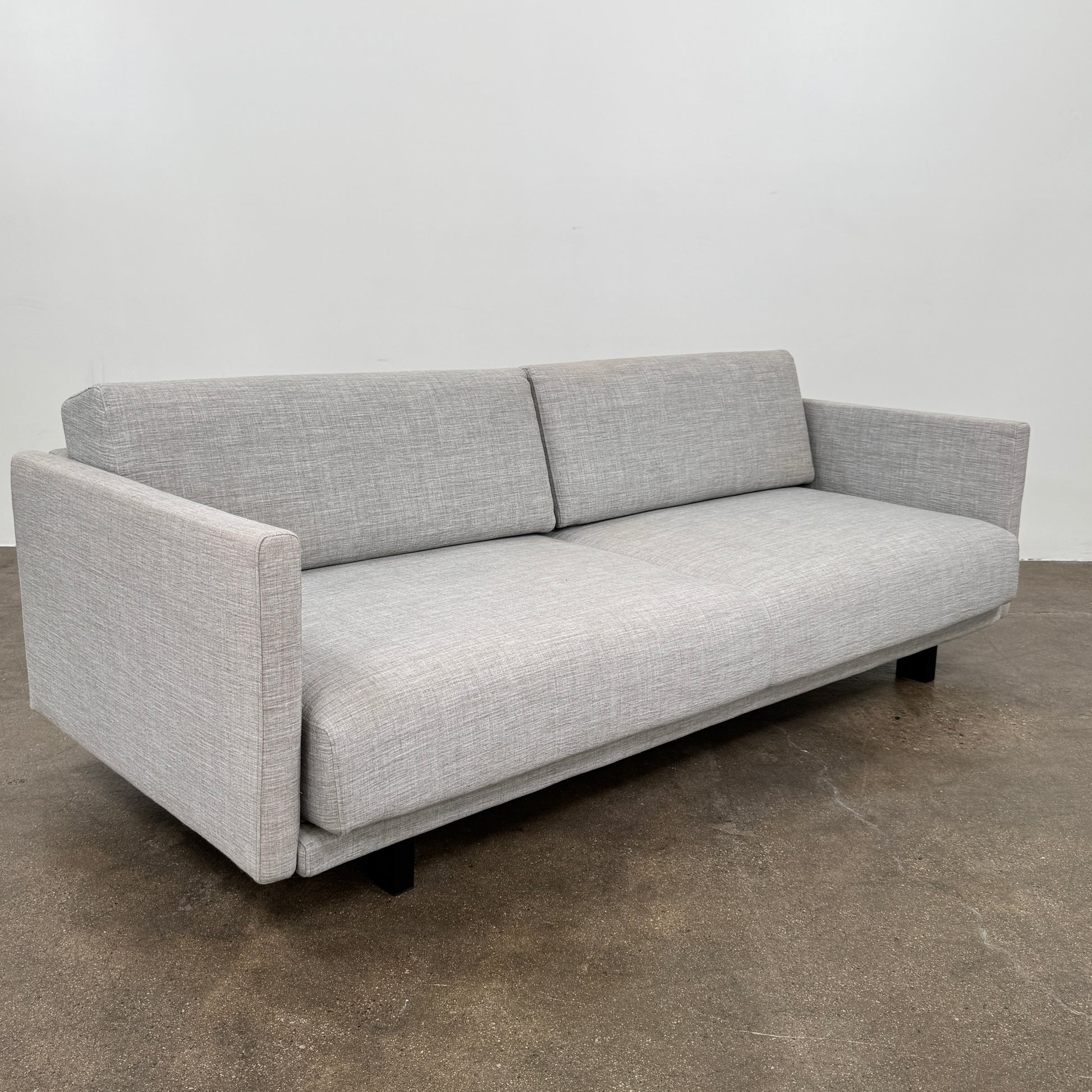 The DWR Tuck Sleeper Sofa by DWR features modern light gray fabric, straight arms, and black legs—ideal for a guest room. Shown against a plain white background.