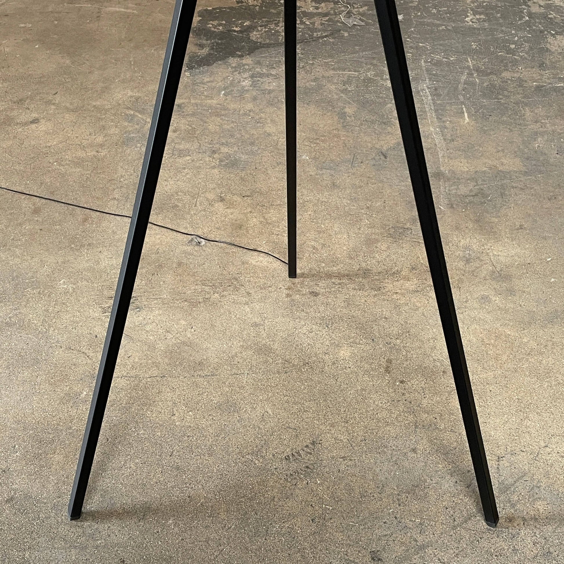 A large circular mirror set in a black metal frame on a tripod stand, isolated against a white background, exudes sophistication akin to the Flos Superloon Floor Light by Flos, providing broad and diffused light that can be dimmed for any ambiance.