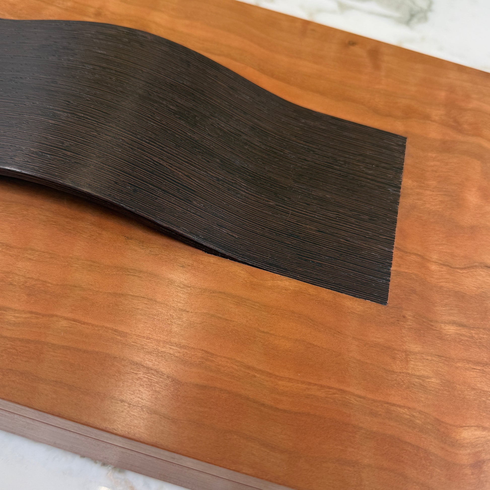 The Mike Fair Jewelry Box / Cigar Box by Mike Fair Custom Furnishings is a rectangular cherry wood box with a smooth finish and a curved, dark handle on the lid, displayed against a plain white background.