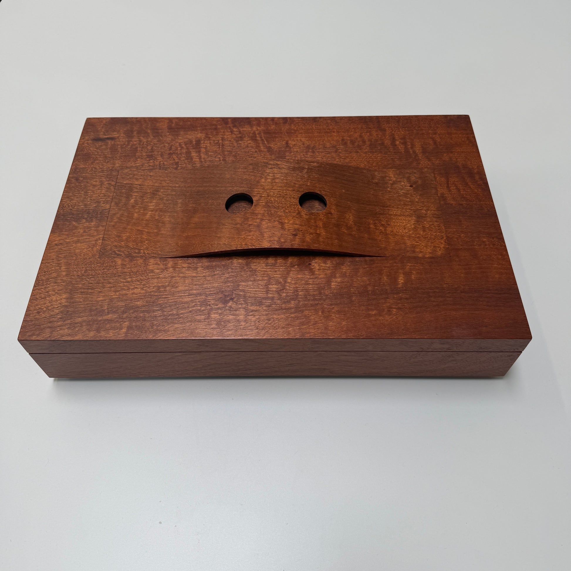 The Mike Fair Jewelry / Cigar Box by Mike Fair Custom Furnishings is a rectangular handcrafted box with a lid featuring a curved cutout and two circular holes, displayed against a plain white background.