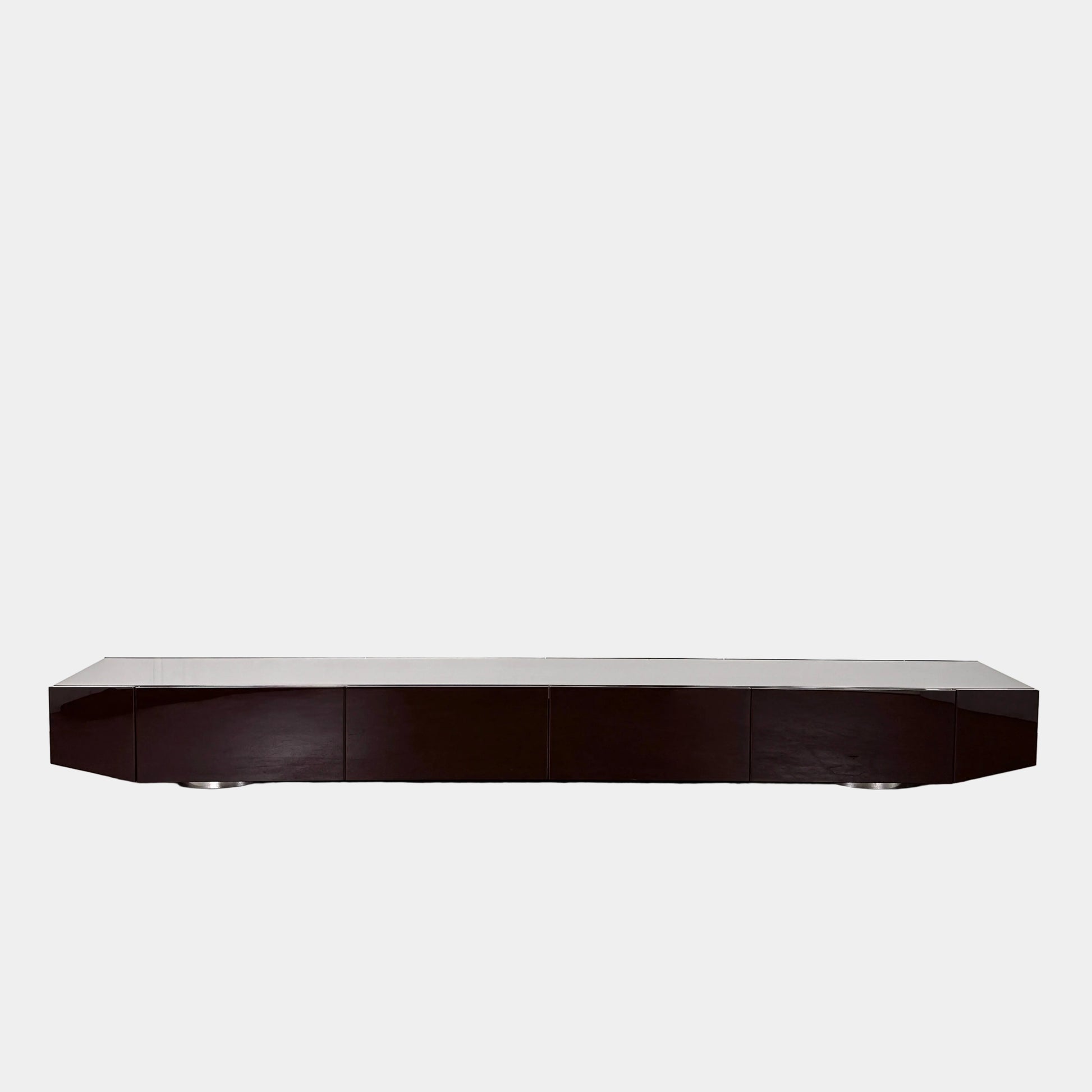 The Minotti Jason Sideboard by Minotti is a long, low-profile, dark brown modern piece with four doors, shown against a white wall on a polished concrete floor.