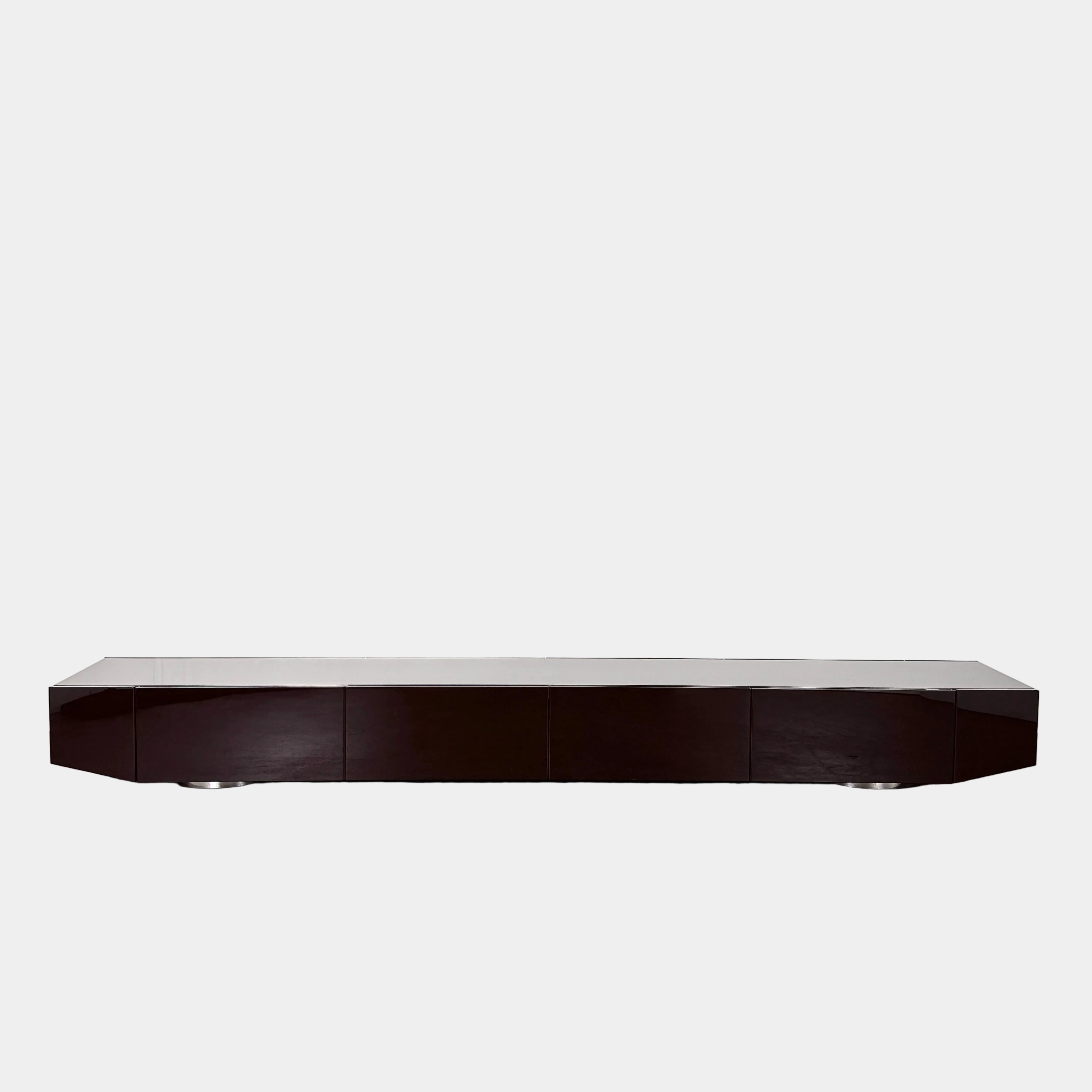 The Minotti Jason Sideboard by Minotti is a long, low-profile, dark brown modern piece with four doors, shown against a white wall on a polished concrete floor.
