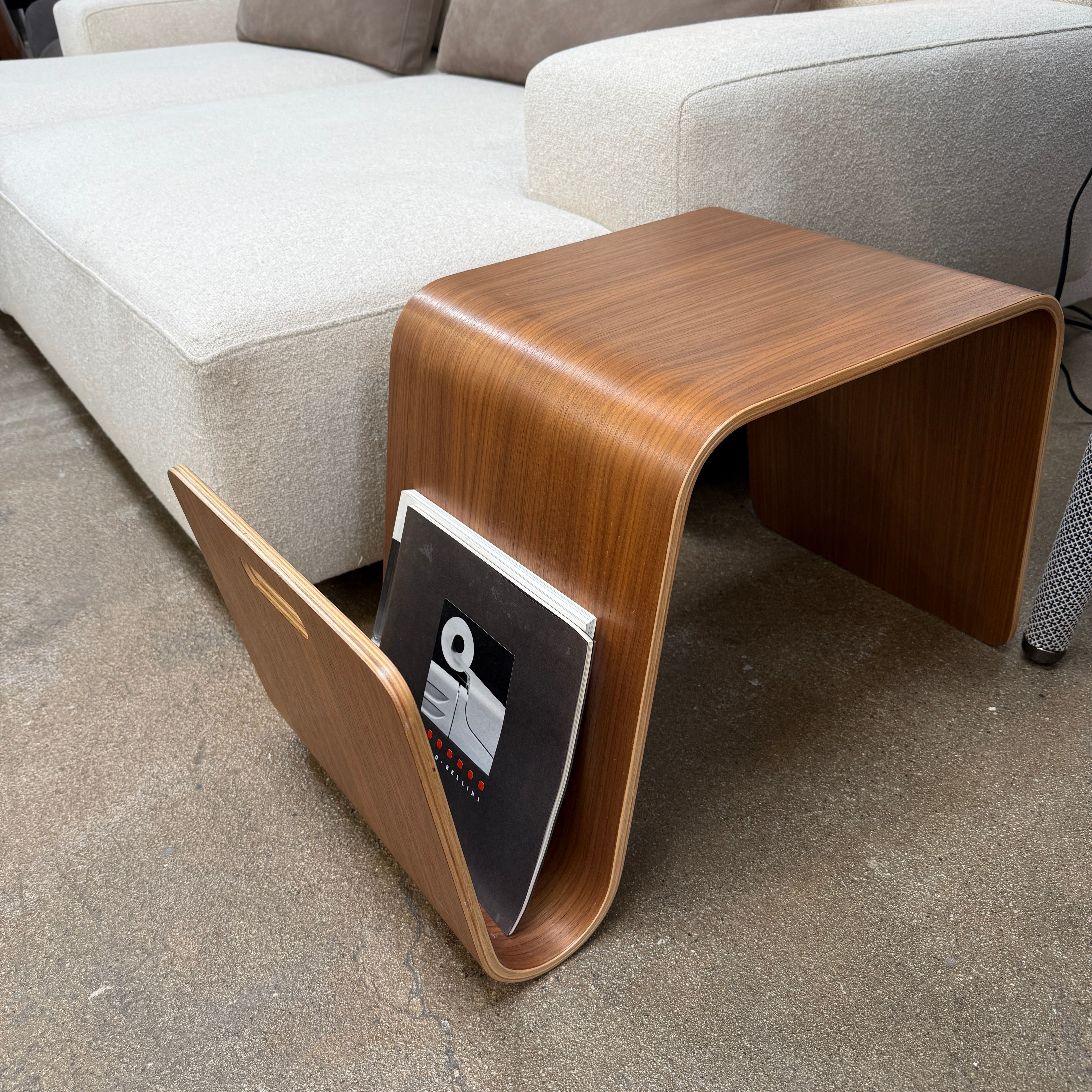 The Offi Mag Table by Offi is a minimalist wooden side table with an angular, wave-inspired design. It serves as a multifunctional table or compact workstation, featuring a curved slot for storage—displayed on a plain white background.