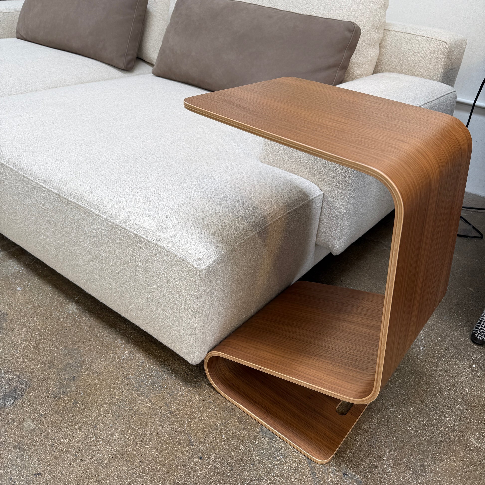 The Offi Mag Table by Offi is a minimalist wooden side table with an angular, wave-inspired design. It serves as a multifunctional table or compact workstation, featuring a curved slot for storage—displayed on a plain white background.
