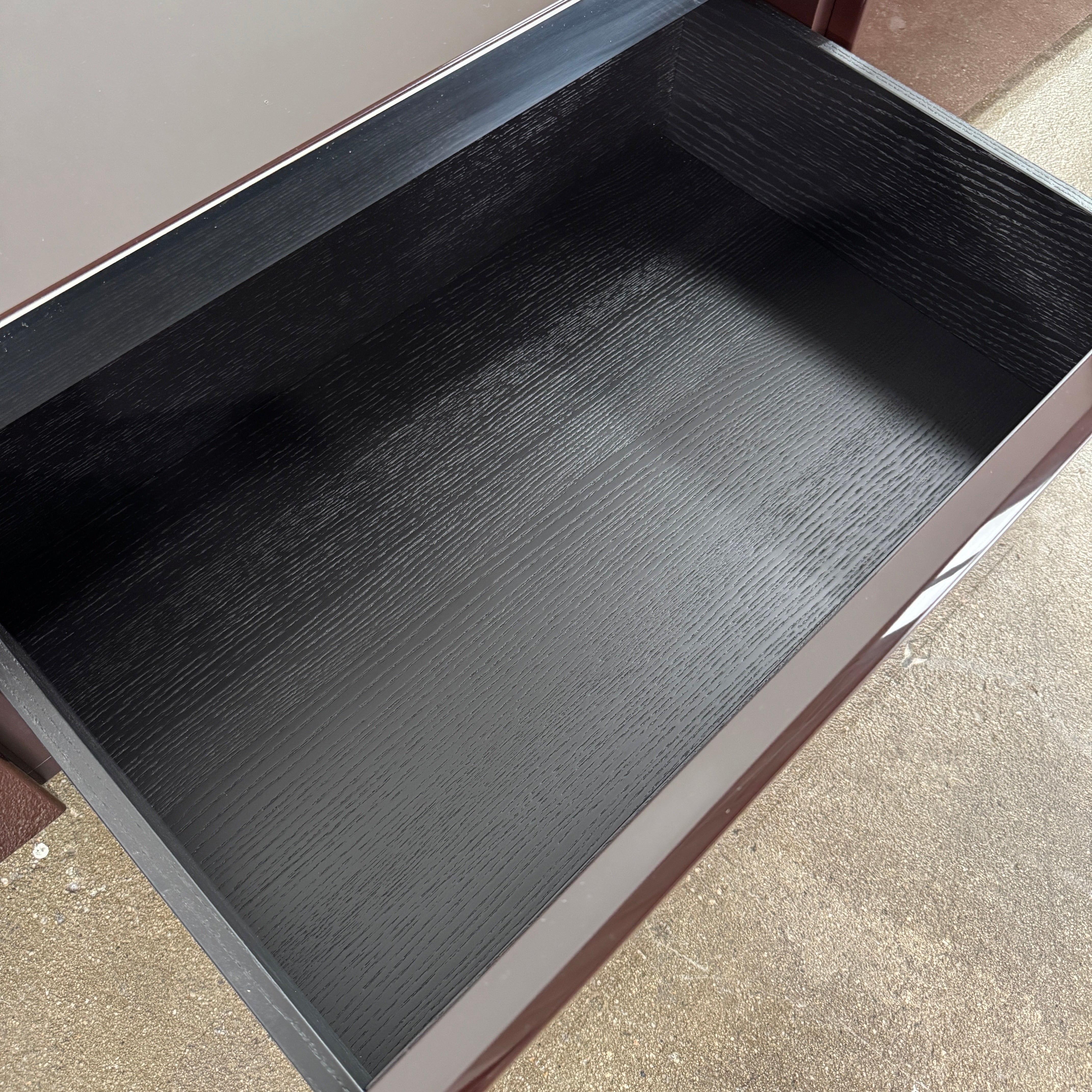 The Minotti Jason Sideboard by Minotti is a long, low-profile, dark brown modern piece with four doors, shown against a white wall on a polished concrete floor.