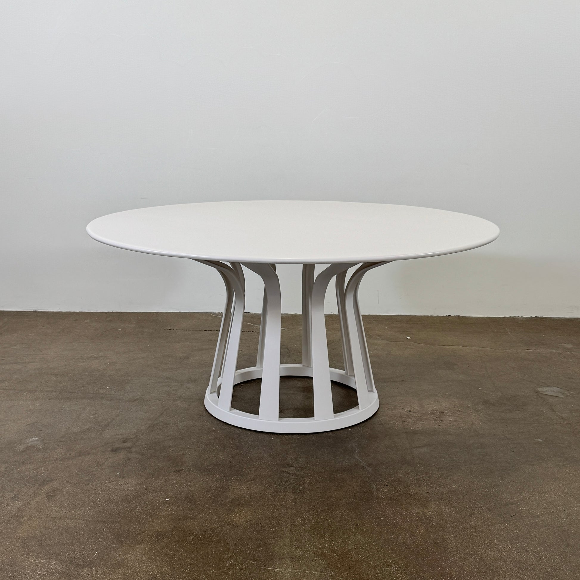 The Cassina Lebeau white outdoor dining table by Modern Resale features a solid round top and an open geometric base, shown on a plain concrete floor against a white wall.