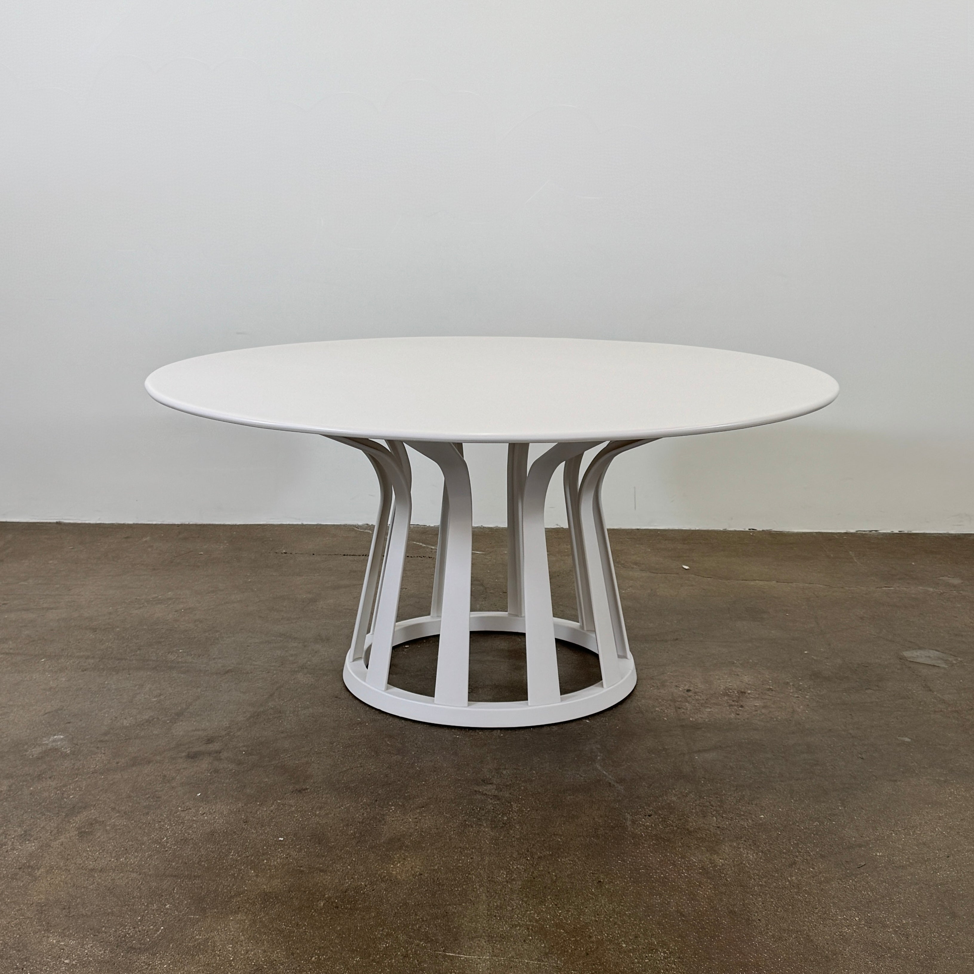 The Cassina Lebeau white outdoor dining table by Modern Resale features a solid round top and an open geometric base, shown on a plain concrete floor against a white wall.