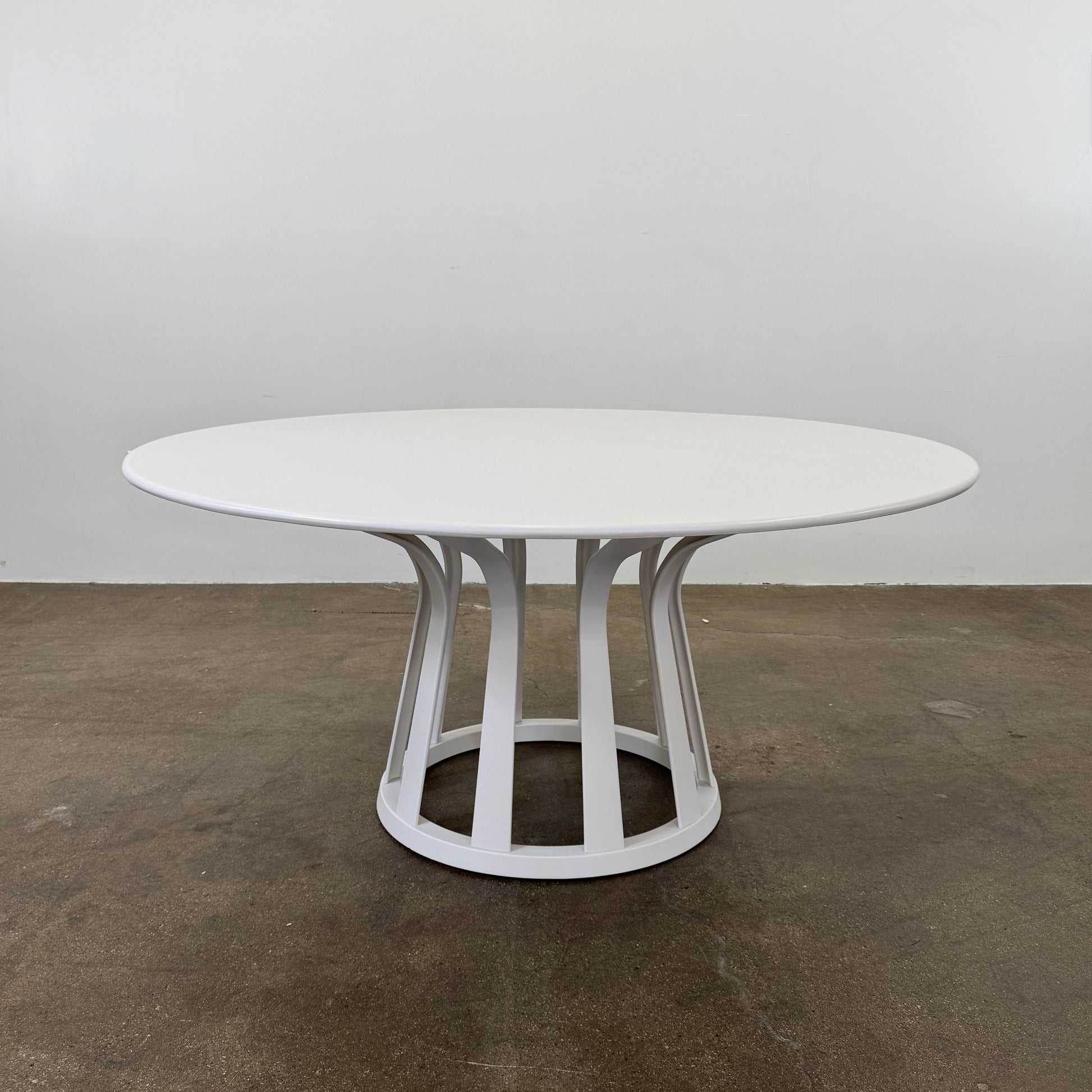 The Cassina Lebeau Outdoor Dining Table by Cassina features a round white porcelain stoneware top and a geometric openwork base, ideal for outdoor dining. Shown on a plain white background.