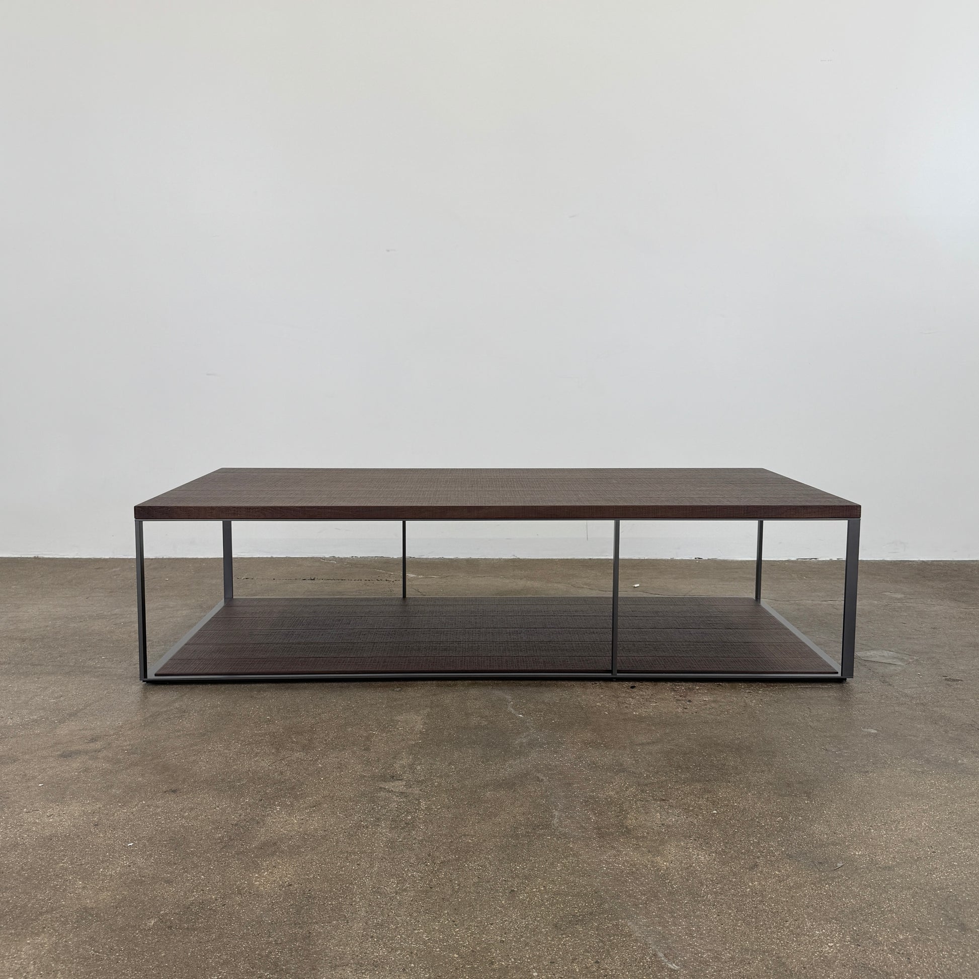 The Maxalto Lithos Coffee Table by Maxalto features a rectangular dark wood top and lower shelf, supported by a minimalist black metal frame, and is displayed against a plain white background.