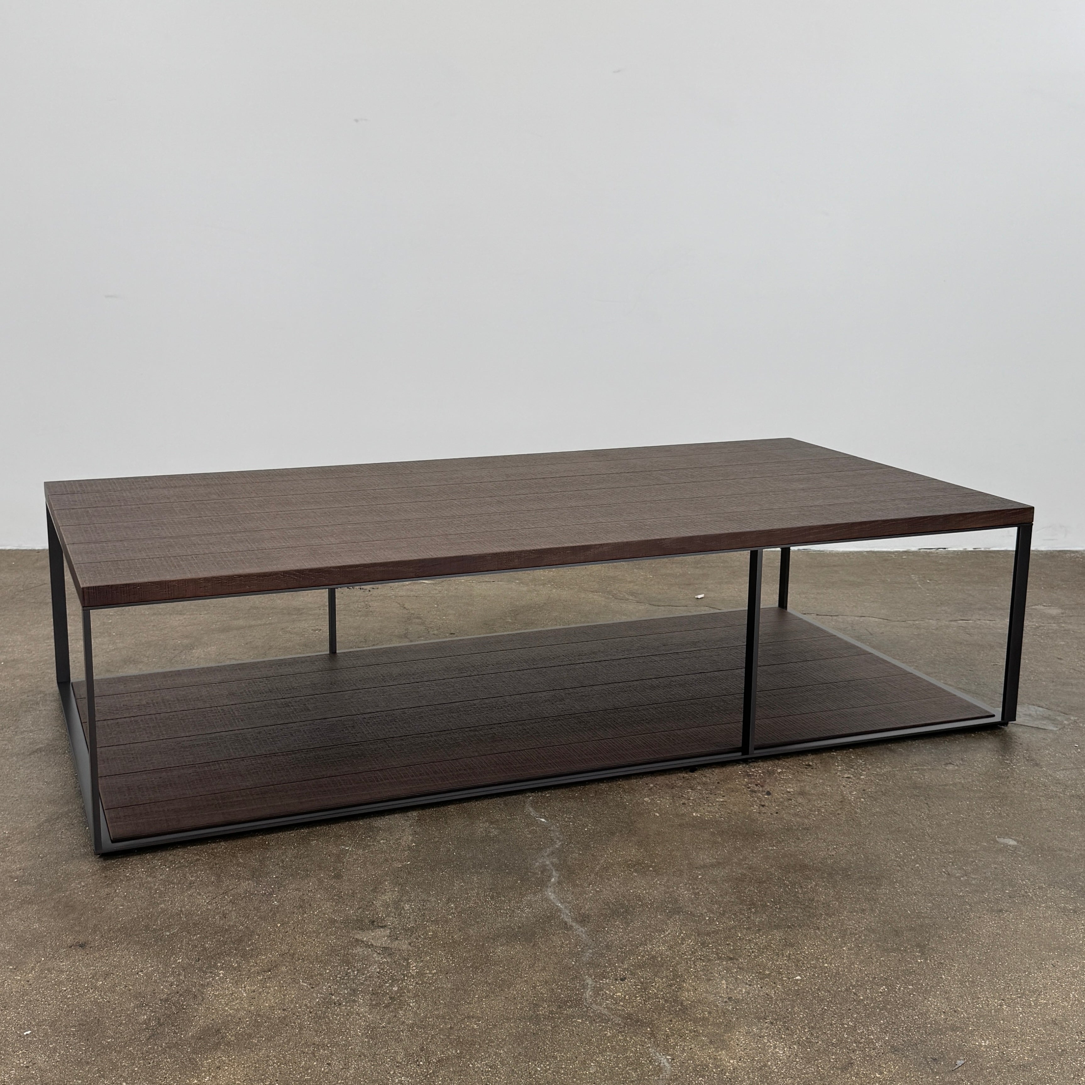 The Maxalto Lithos Coffee Table by Maxalto features a rectangular dark wood top and lower shelf, supported by a minimalist black metal frame, and is displayed against a plain white background.