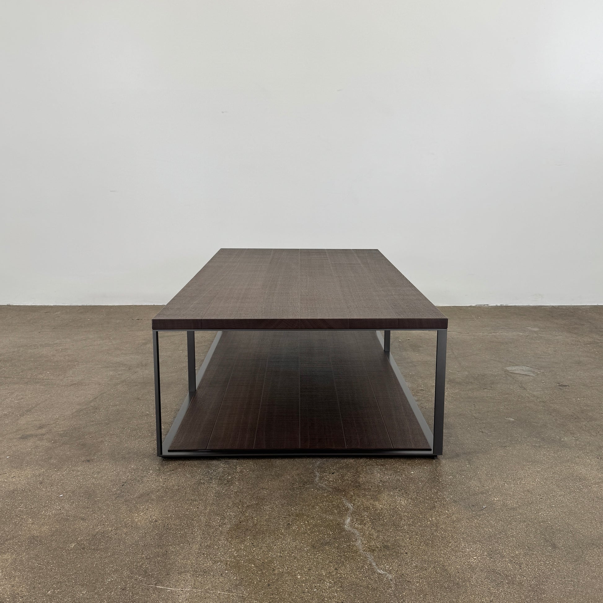 The Maxalto Lithos Coffee Table by Maxalto features a rectangular dark wood top and lower shelf, supported by a minimalist black metal frame, and is displayed against a plain white background.