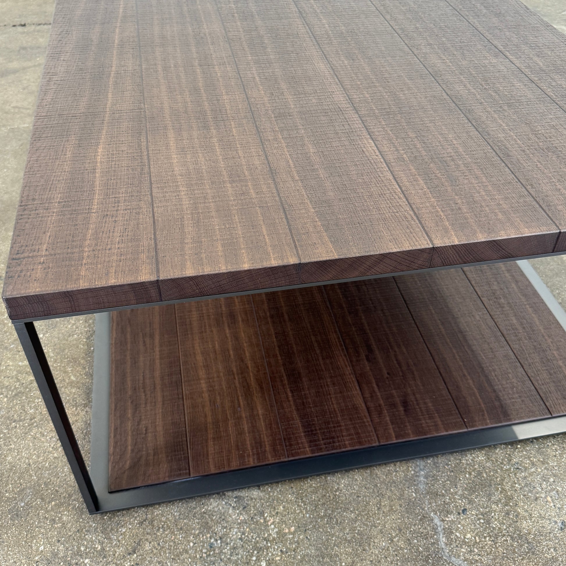 The Maxalto Lithos Coffee Table by Maxalto features a rectangular dark wood top and lower shelf, supported by a minimalist black metal frame, and is displayed against a plain white background.