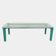 The B&B Italia Oskar Dining Table by B&B Italia features a rectangular glass top with four teal legs, displayed against a plain white background.