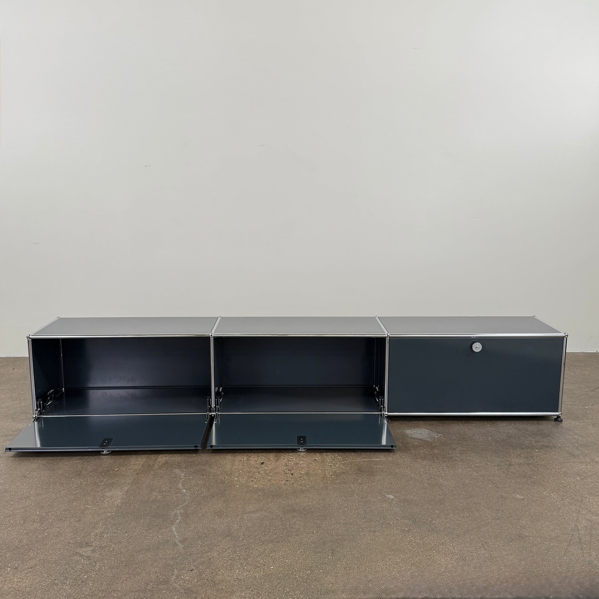 The USM Haller Low Console - Three Flap Door Unit features three black flap doors with round knobs and a silver frame, shown against a plain white background.