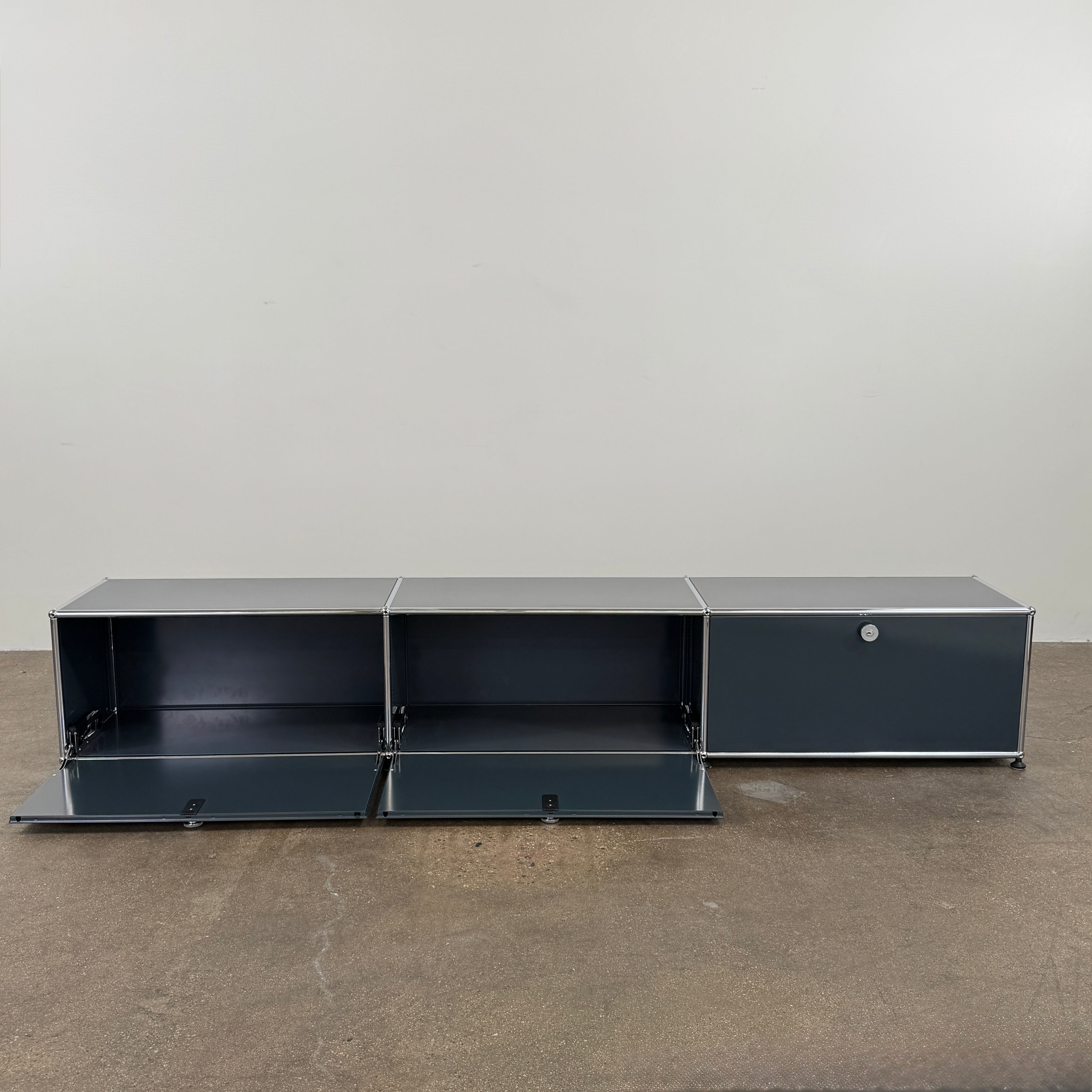 The USM Haller Low Console - Three Flap Door Unit features three black flap doors with round knobs and a silver frame, shown against a plain white background.