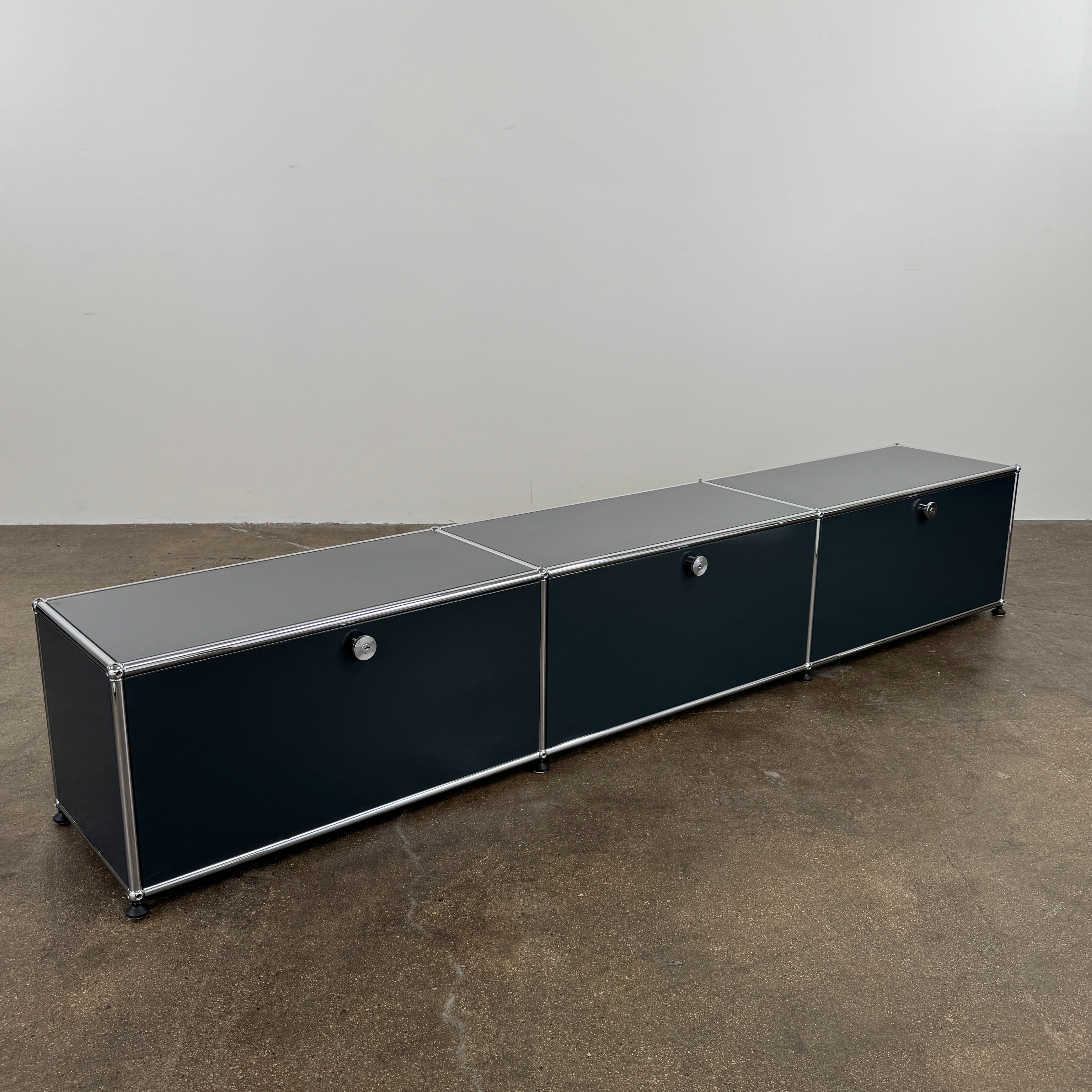 The USM Haller Low Console - Three Flap Door Unit features three black flap doors with round knobs and a silver frame, shown against a plain white background.