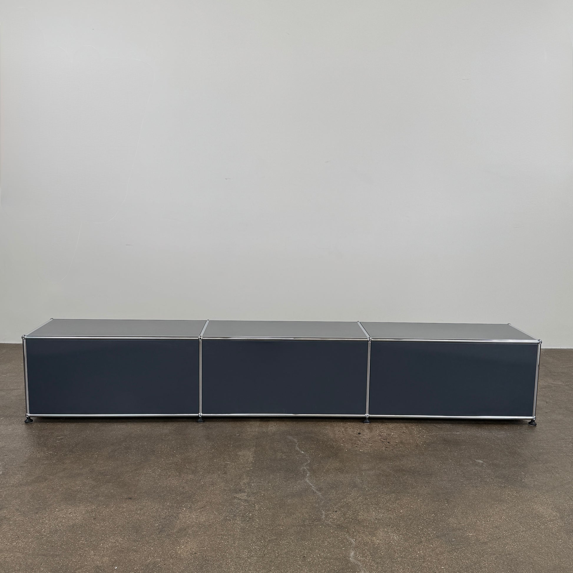 The USM Haller Low Console - Three Flap Door Unit features three black flap doors with round knobs and a silver frame, shown against a plain white background.
